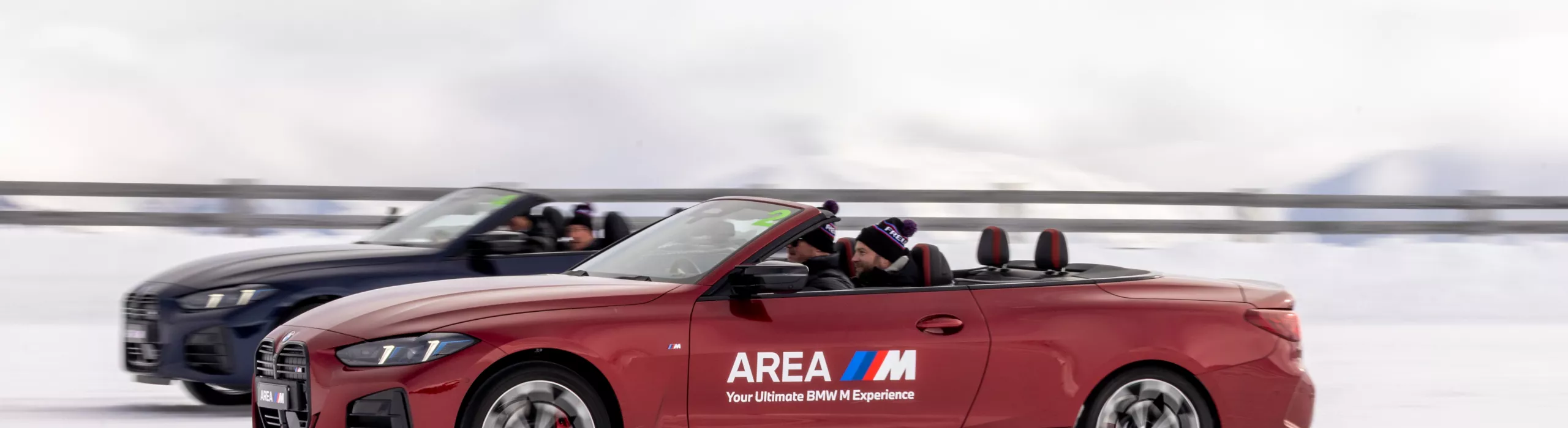 Side profile action shot of a red fire-metallic BMW 4 Series Convertible featuring custom "Area M" livery. Australian drivers master extreme precision car handling, winter cornering maneuvers, and high-speed drift slaloms on specialized snow tracks.