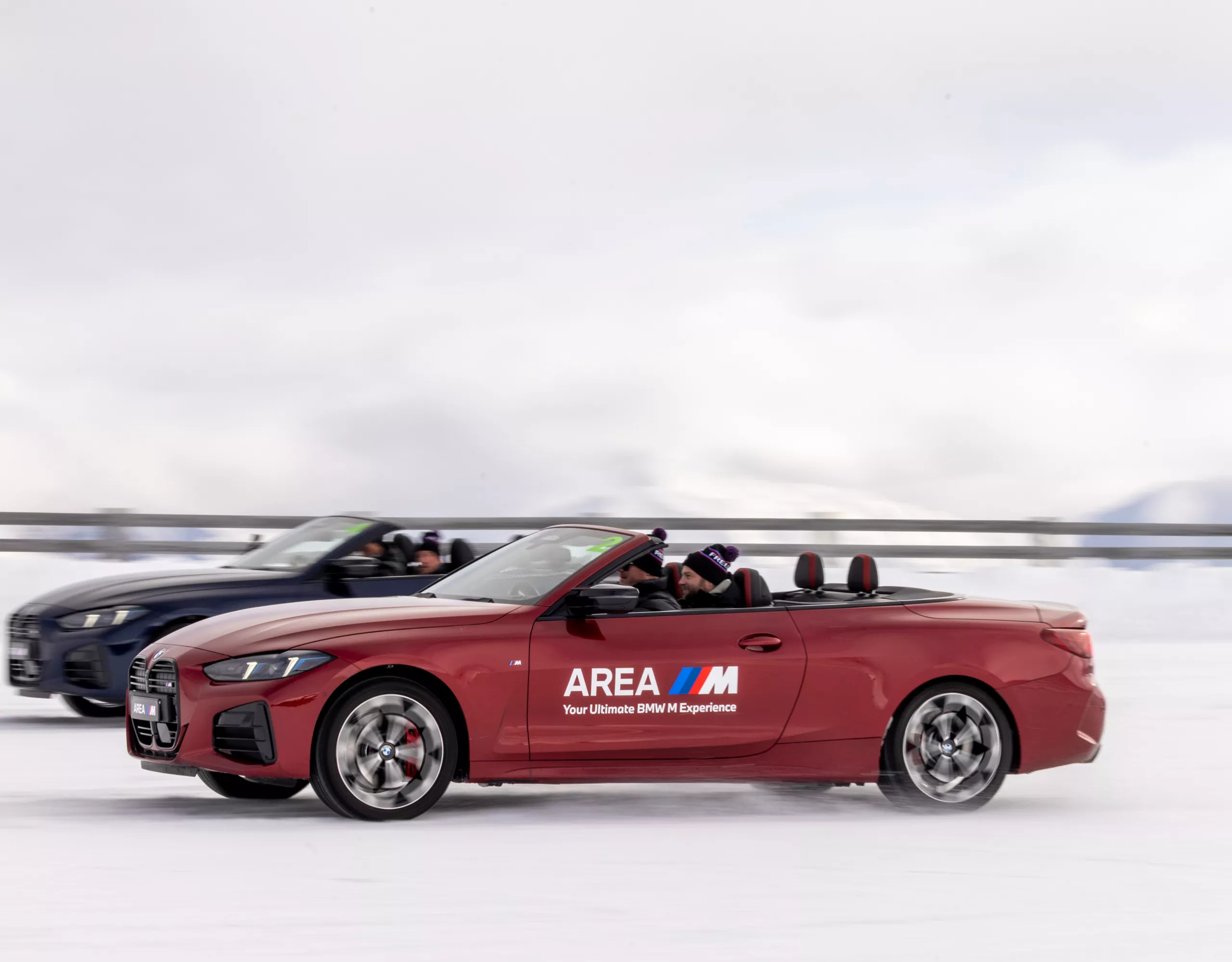 Side profile action shot of a red fire-metallic BMW 4 Series Convertible featuring custom "Area M" livery. Australian drivers master extreme precision car handling, winter cornering maneuvers, and high-speed drift slaloms on specialized snow tracks.