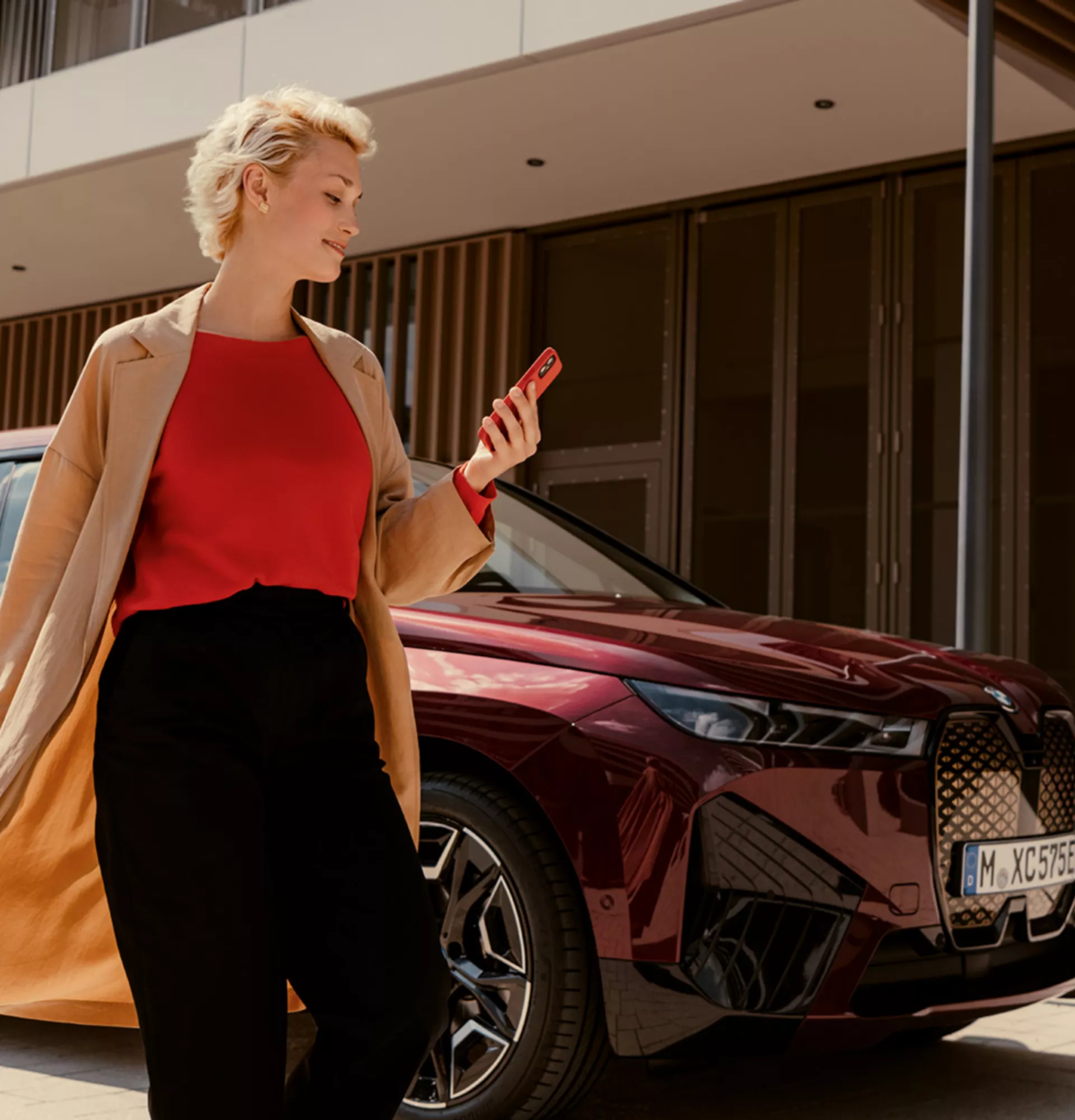 Woman in front of BWW iX uses My BMW app on smartphone