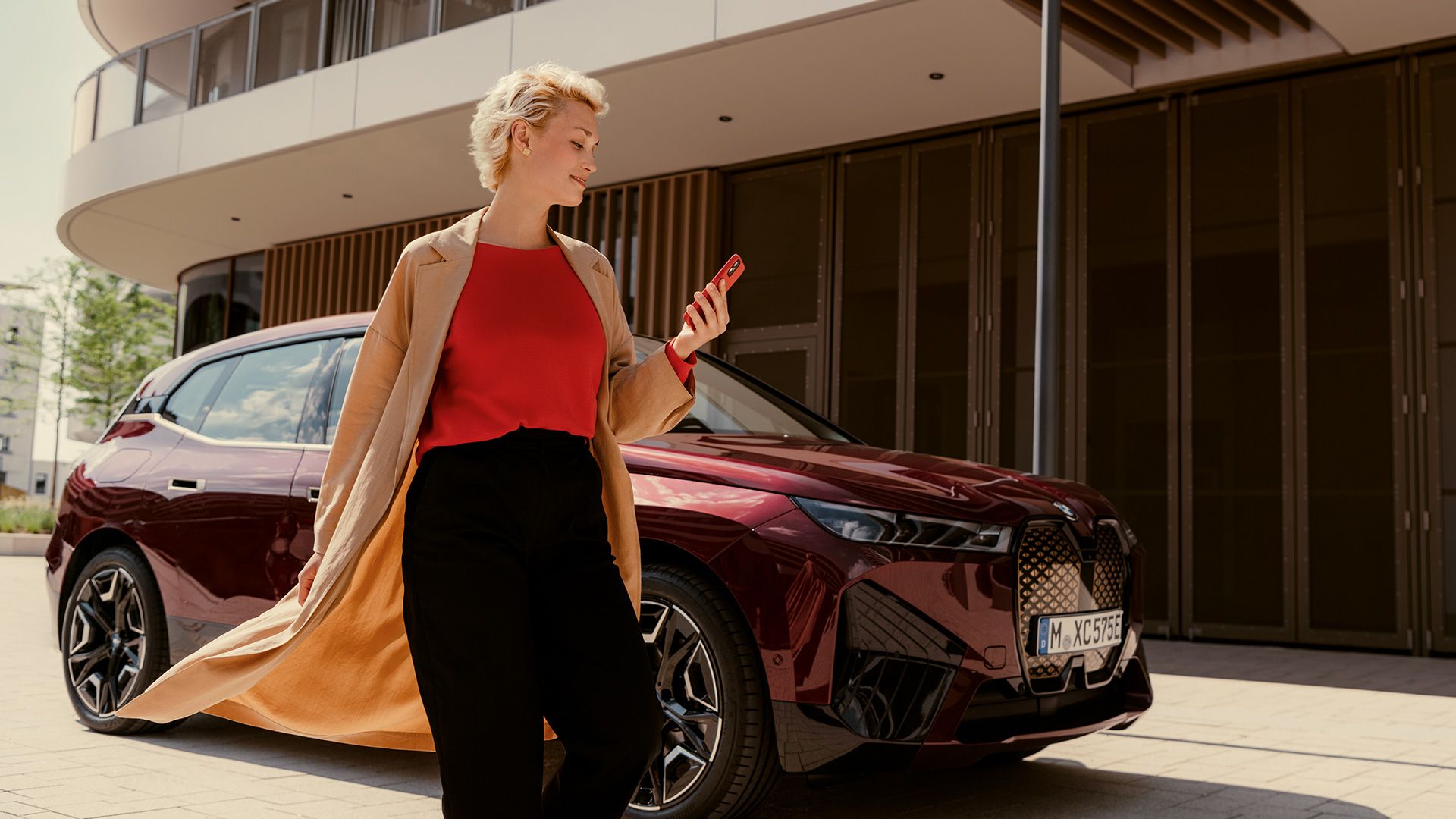 Woman in front of BWW iX uses My BMW app on smartphone