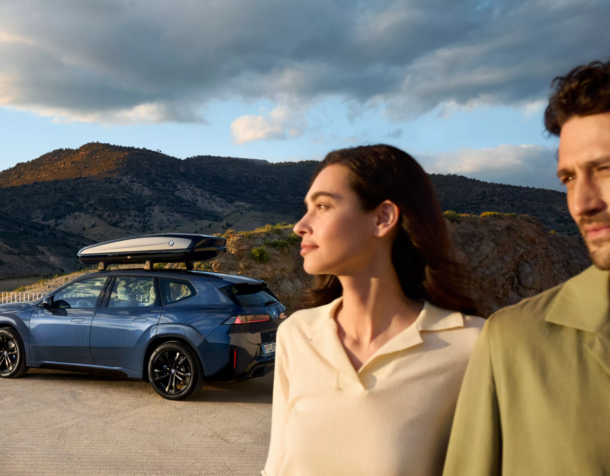 Una coppia davanti a una BMW iX3 su una piattaforma con le montagne sullo sfondo