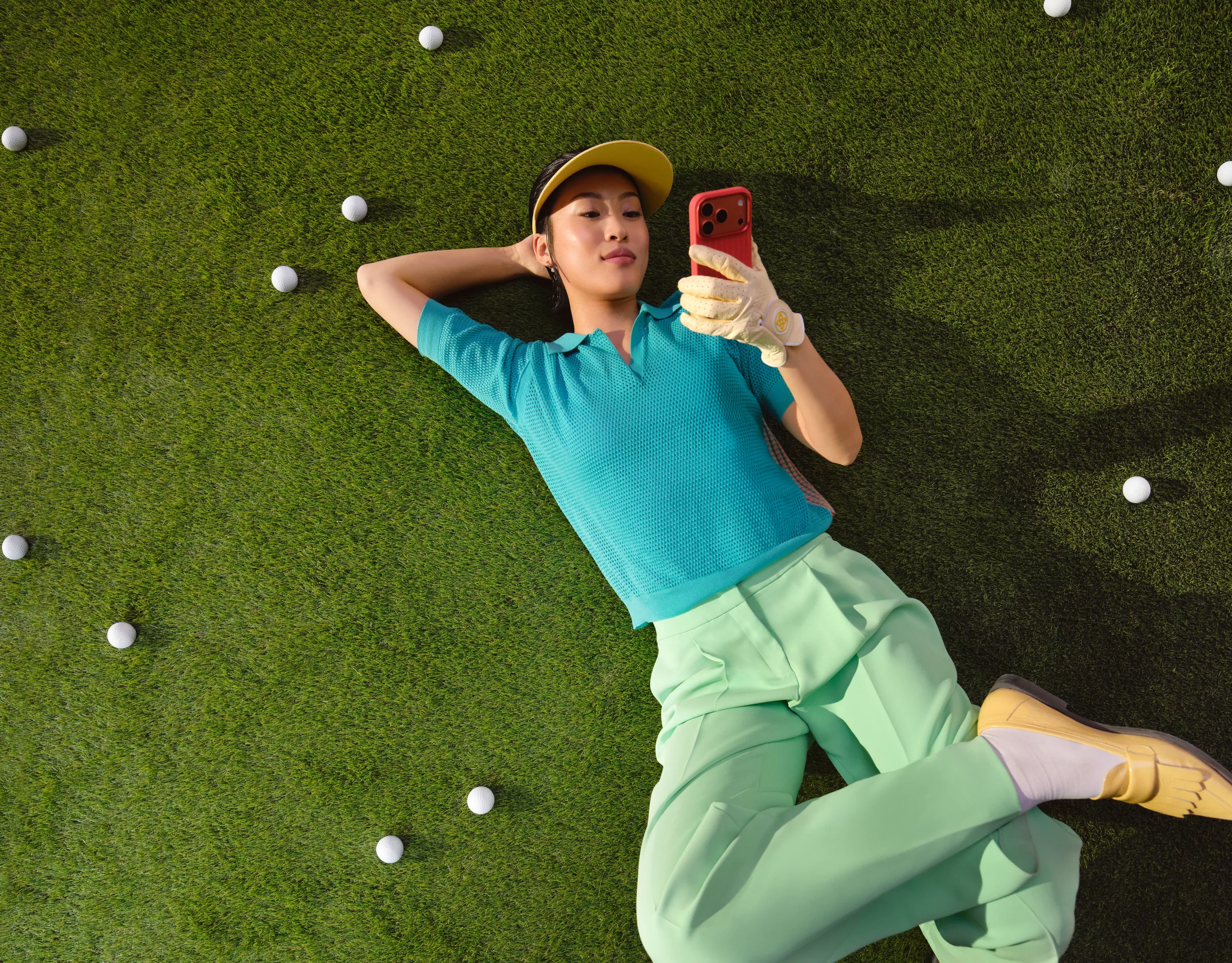 A woman is lying in a meadow with a smartphone in her hand, surrounded by golf balls