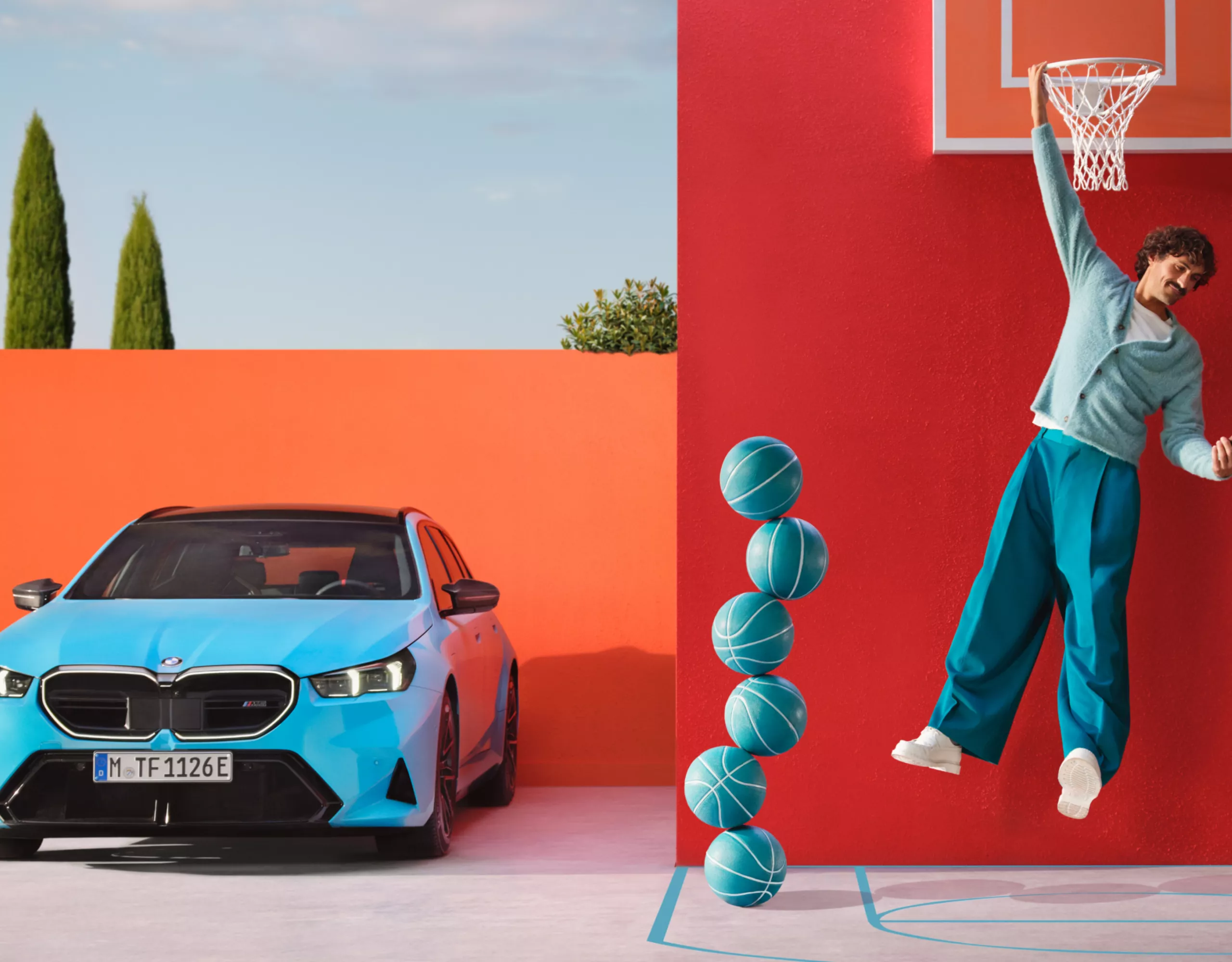 Uomo vestito di blu appeso a un canestro da basket davanti a una parete rossa