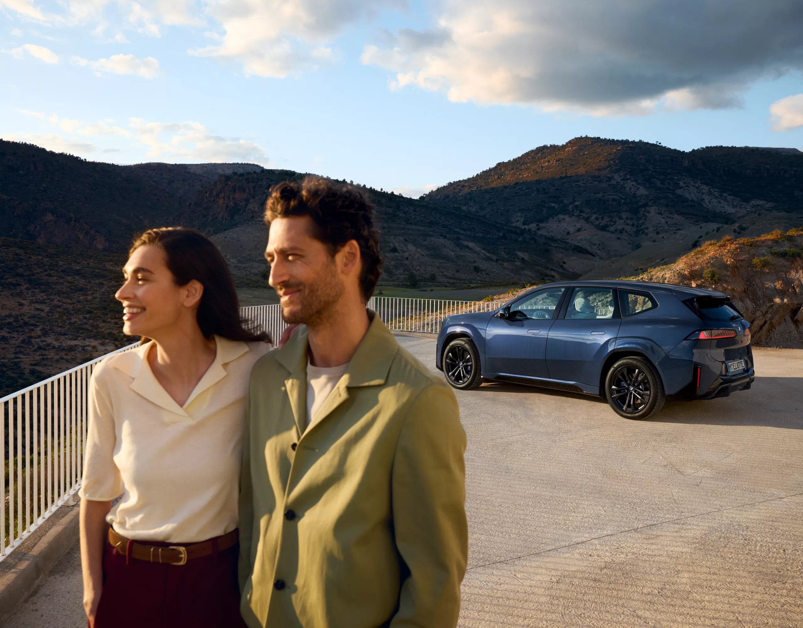 Un couple se tient devant une BMW iX3 sur une plate-forme, avec les montagnes en arrière-plan