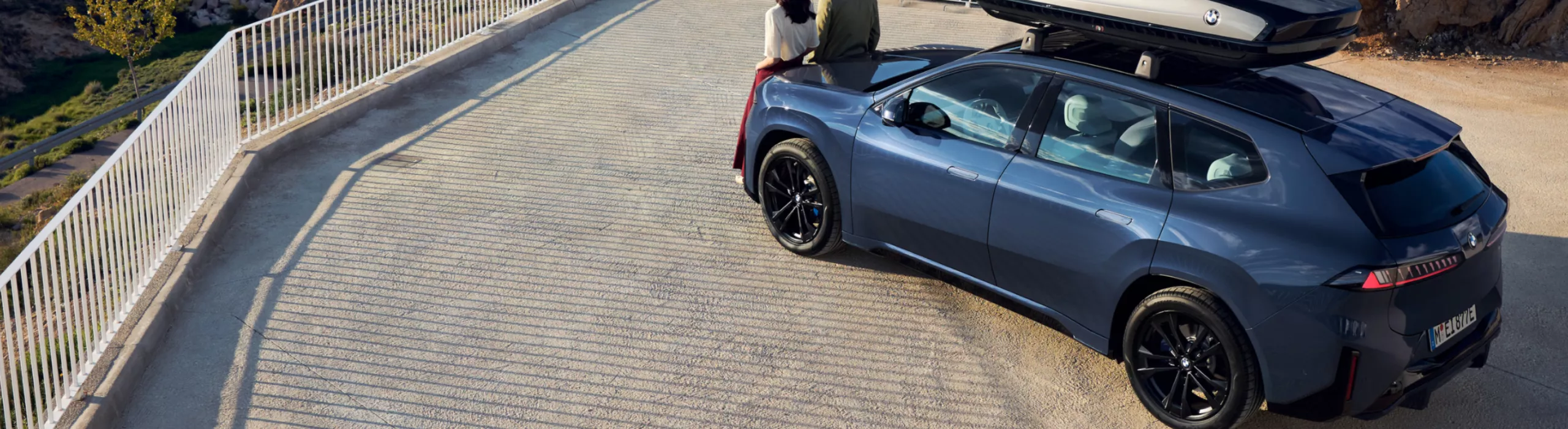 Una coppietta davanti a una BMW iX3 su una terrazza panoramica in montagna
