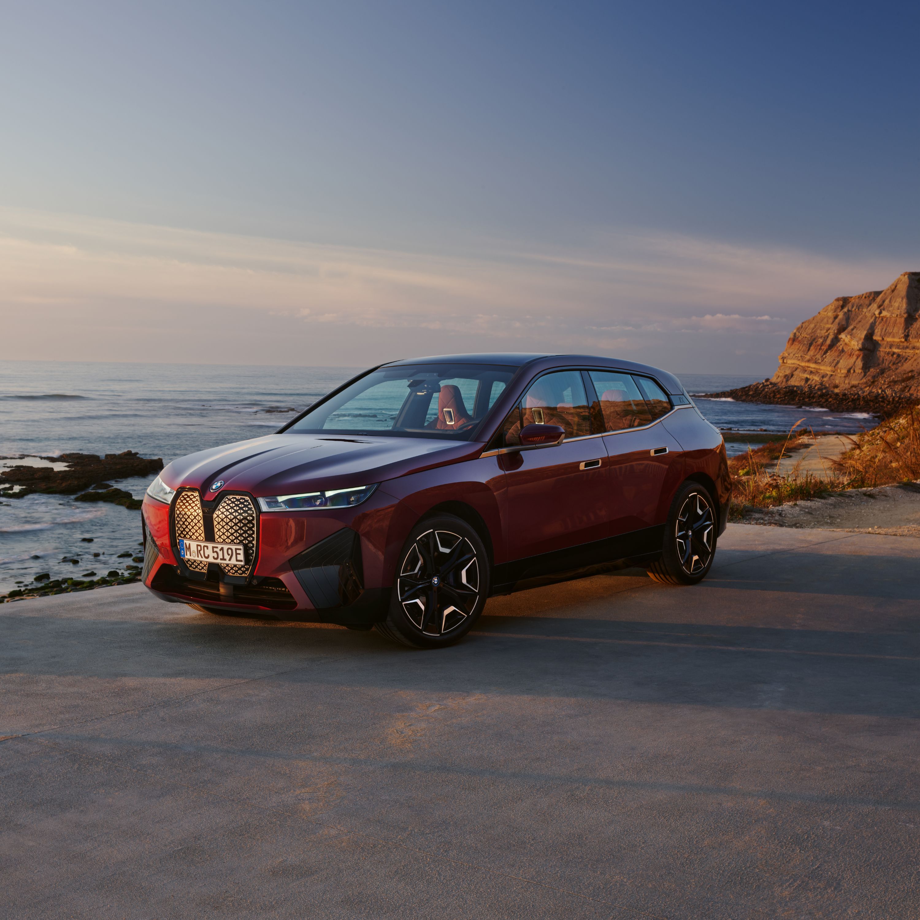 BMW iX i20 parcheggiata davanti a una scogliera con sfondo marino durante la bassa marea al tramonto