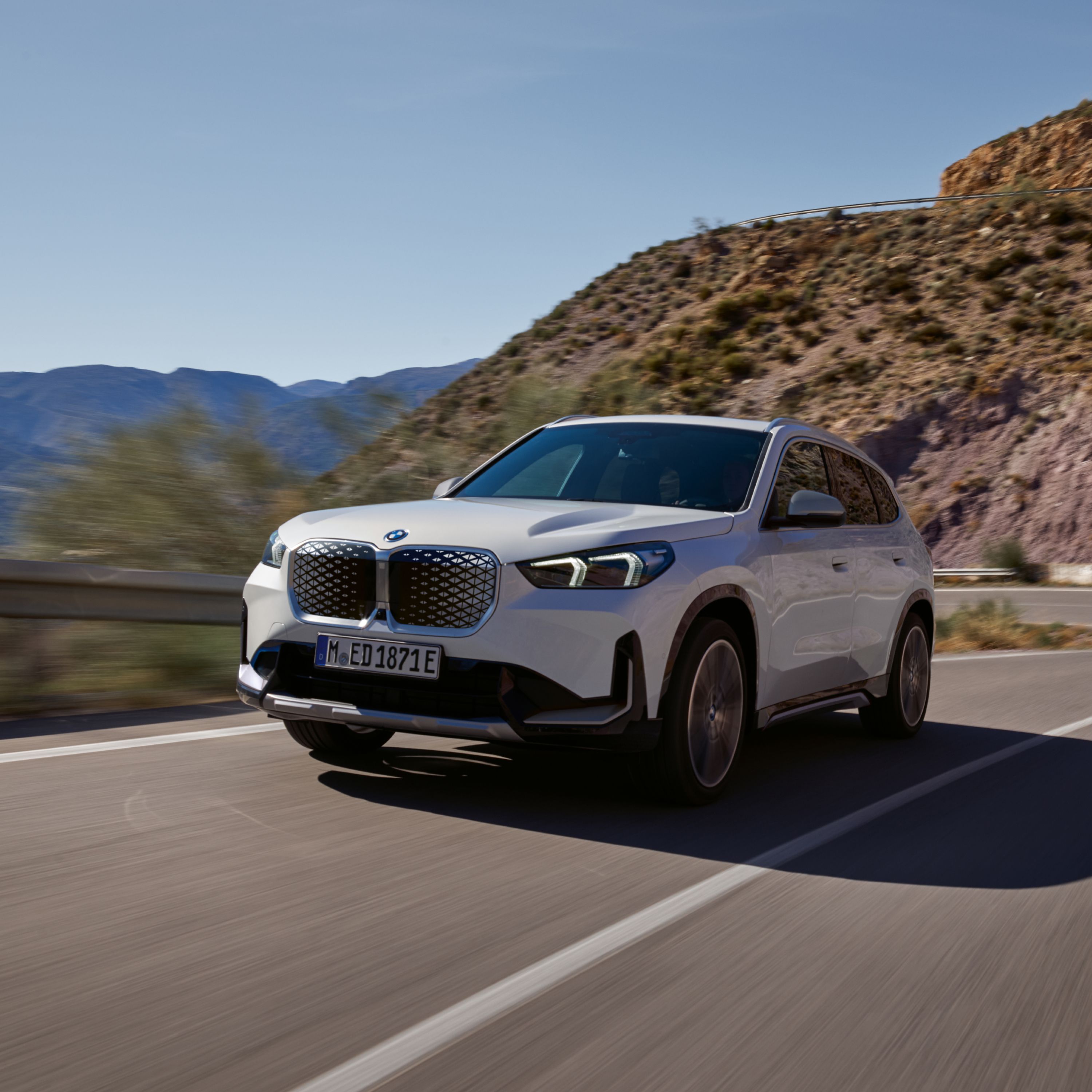 BMW iX1 U11 BEV in white on a serpentine road in a rocky mountain area