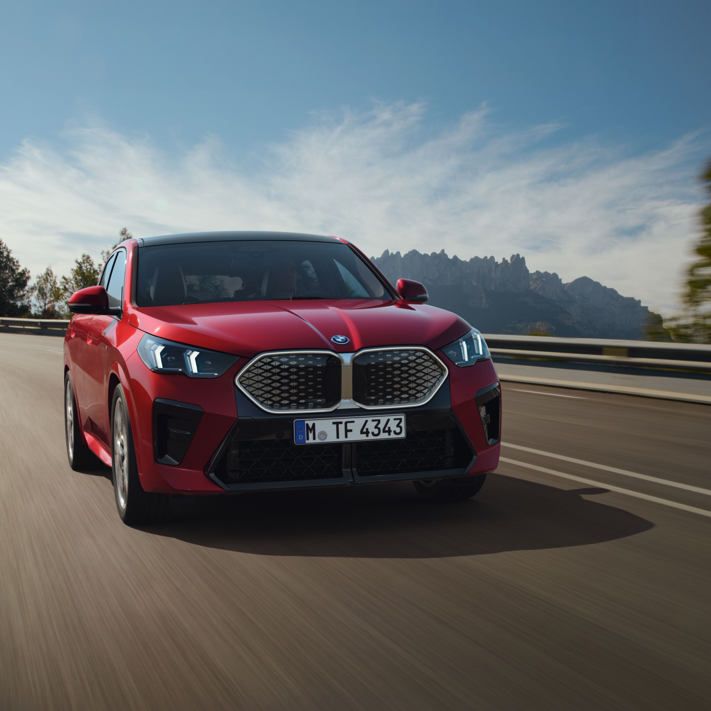 BMW iX2 U10 SUV on a highway in front of a forested mountain panorama