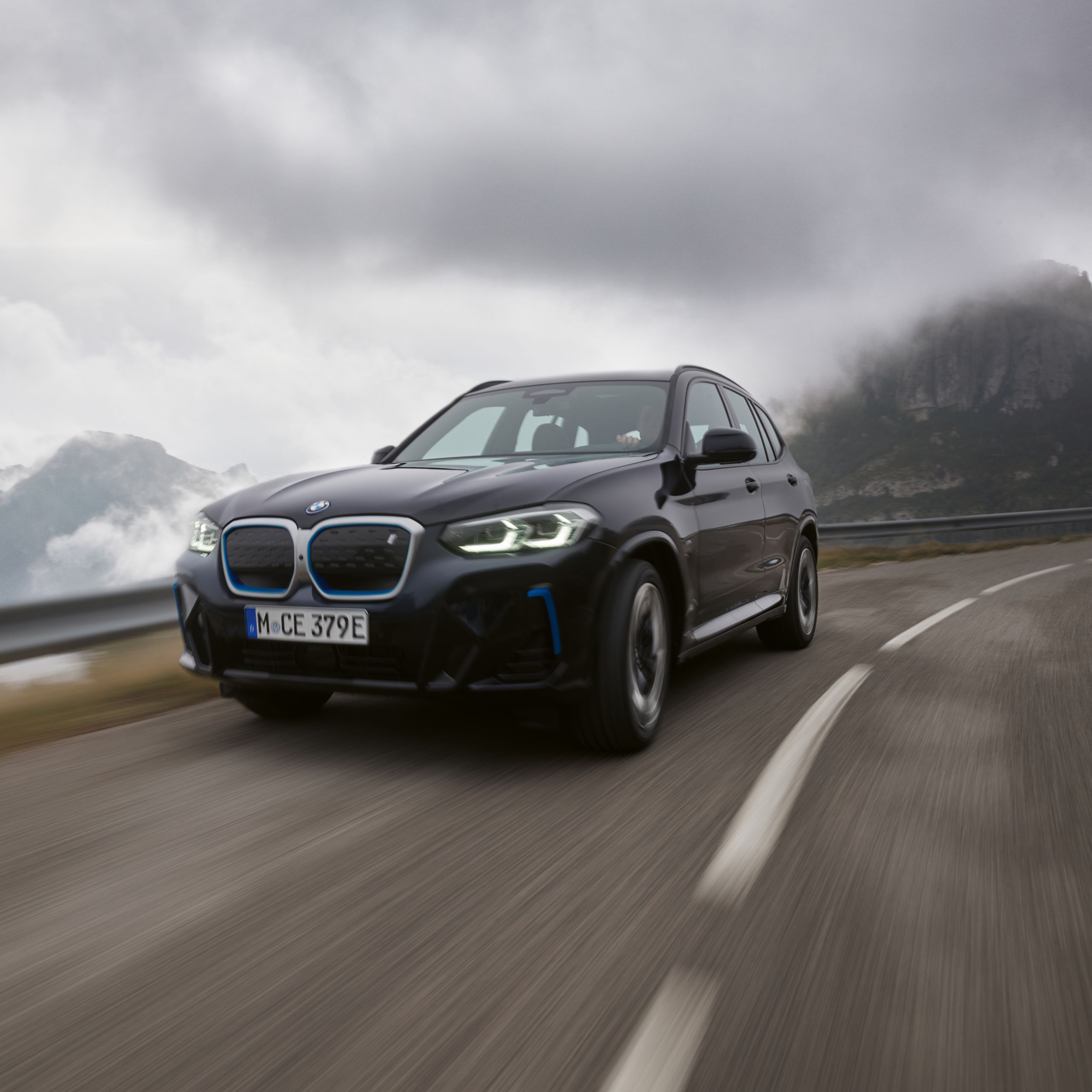 BMW iX3 G08 SUV surrounded by storm clouds on a mountain pass