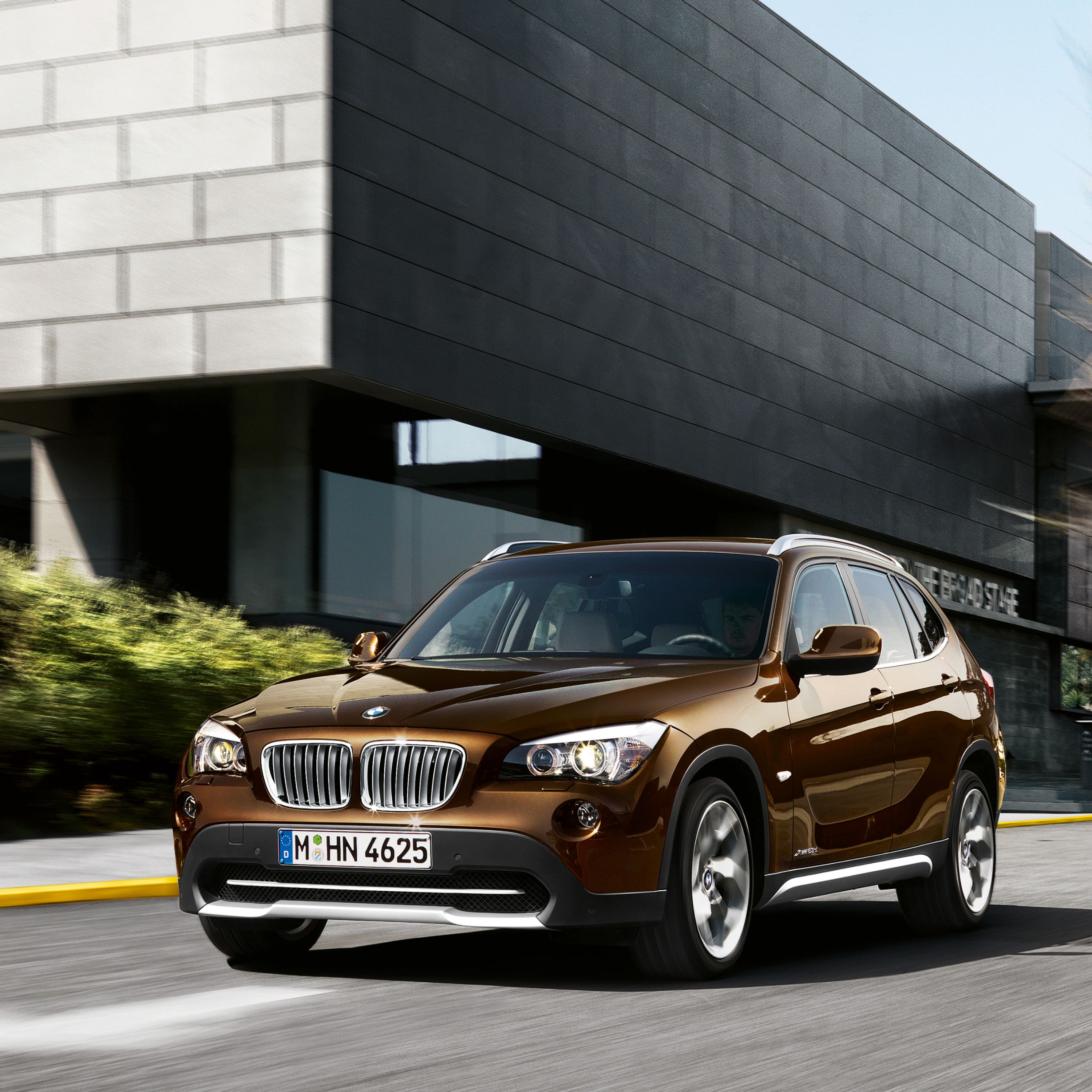 BMW X1 E84 SUV driving on a road in the center of a modern town