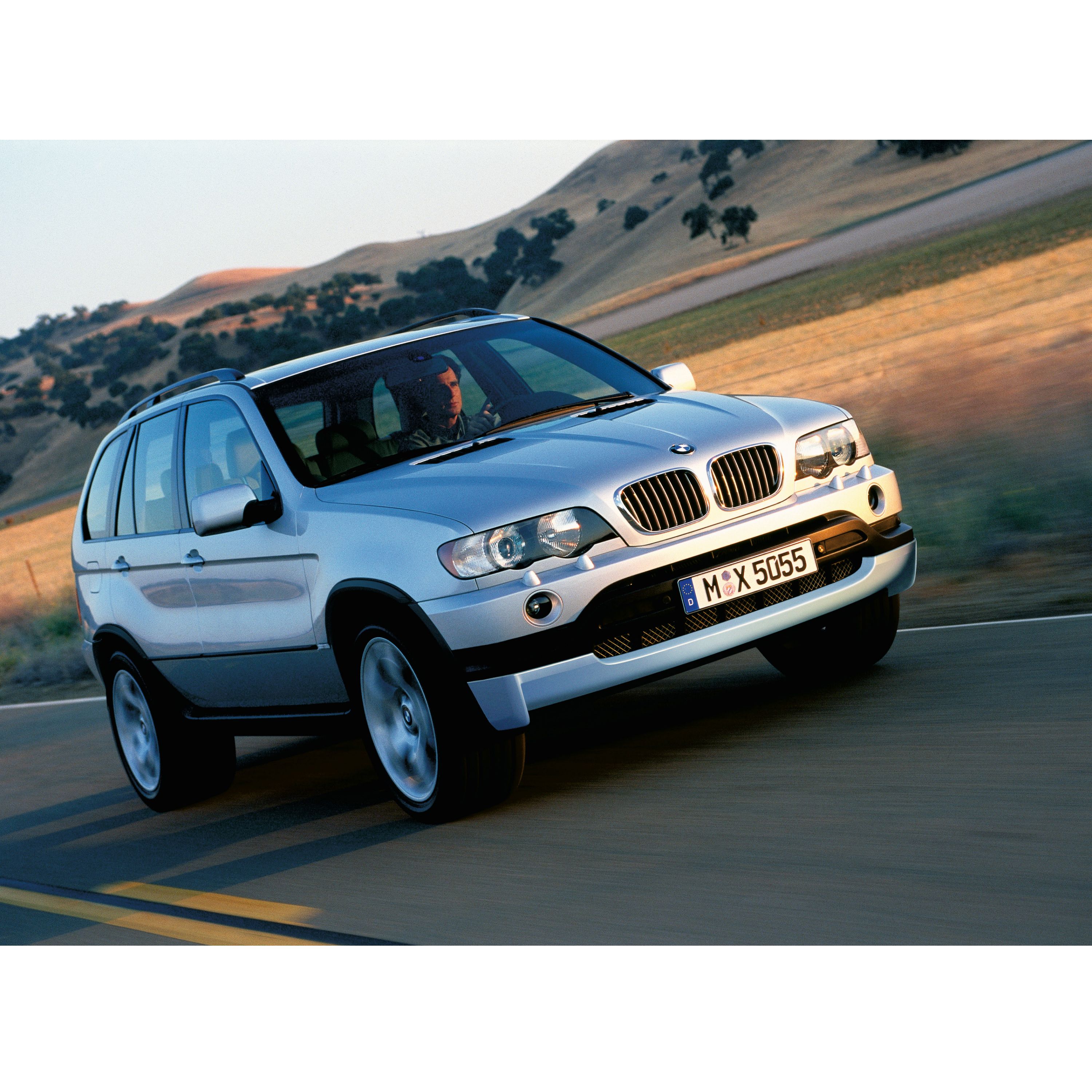 BMW X5 E53 SUV in movimento su una strada di campagna lungo campi di grano