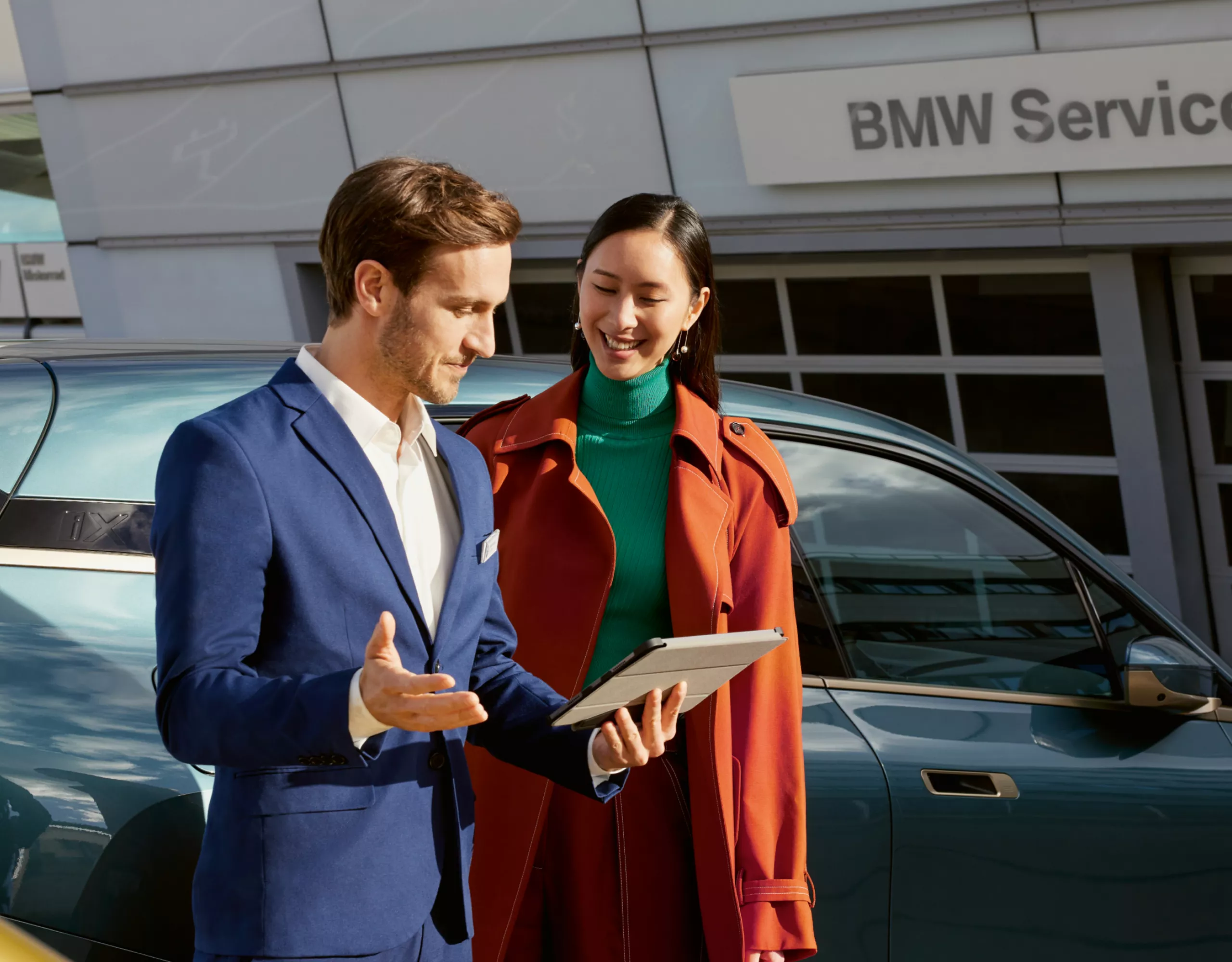 Service BMW, un homme et une femme devant une BMW iX chez le partenaire de service BMW