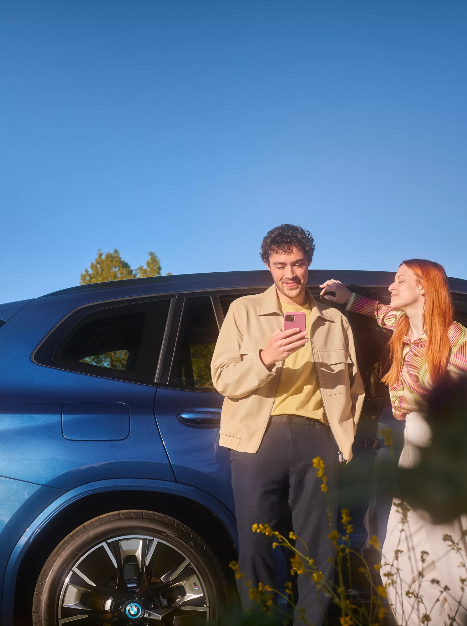 Мъж и жена стоят до син автомобил BMW на открито под ясно синьо небе