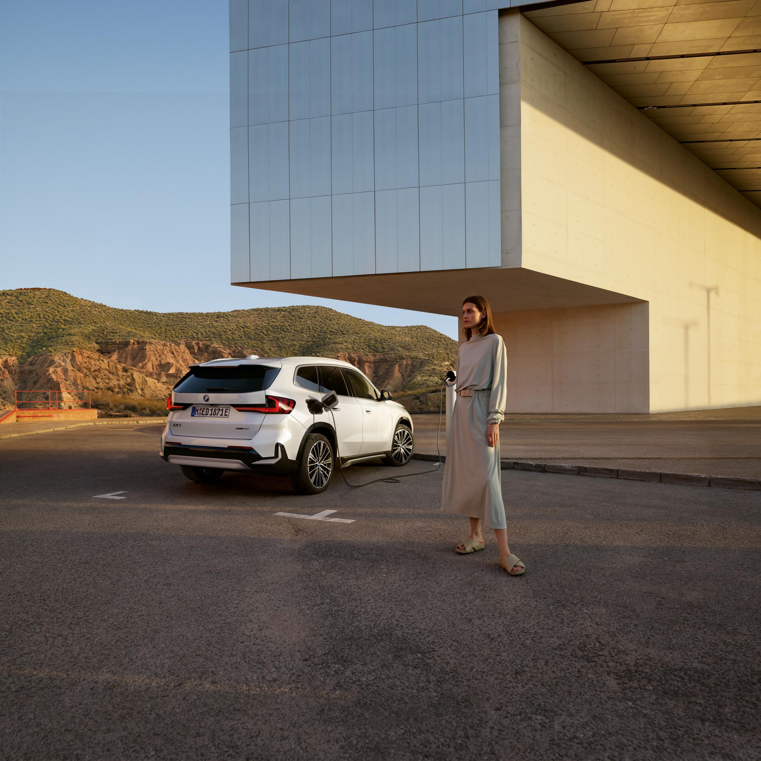 En  kvinna står bredvid en vit BMW iX1 vid en laddstation. 