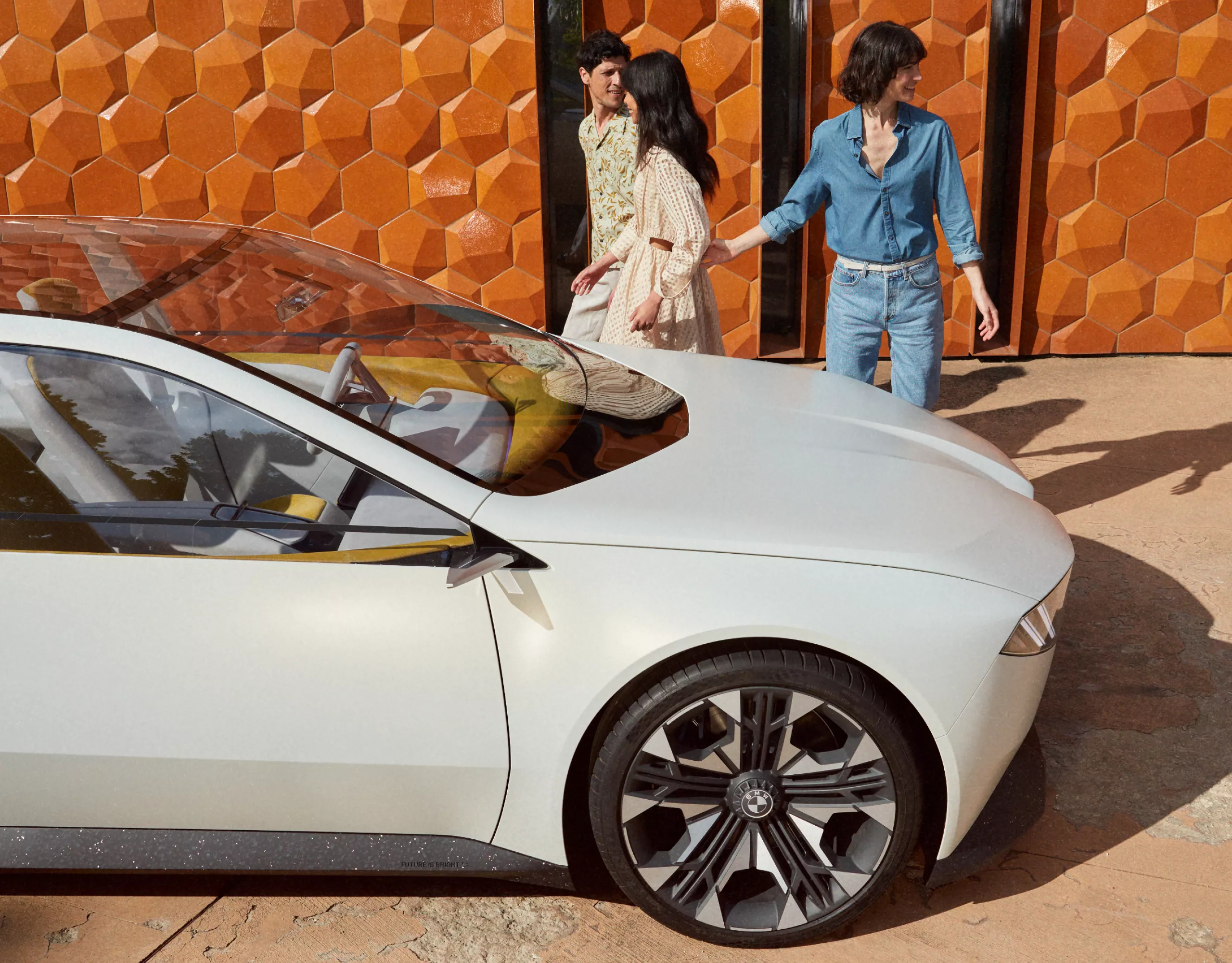 Visão lateral do carro-conceito BMW Vision Neue Klasse 2023, estacionado em frente à parede, com 3 pessoas