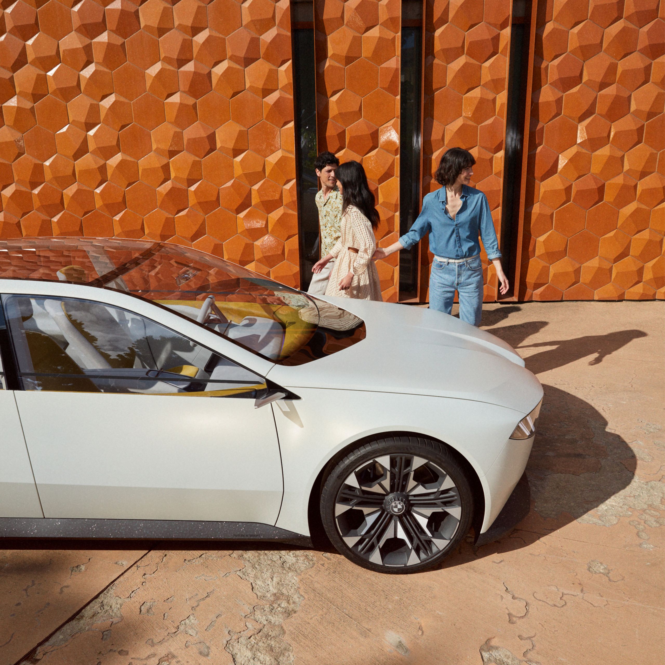 BMW Vision Neue Klasse koncepcióautó 2023, egy fal előtt álló, 3 személy társaságában látható autó oldalnézetből