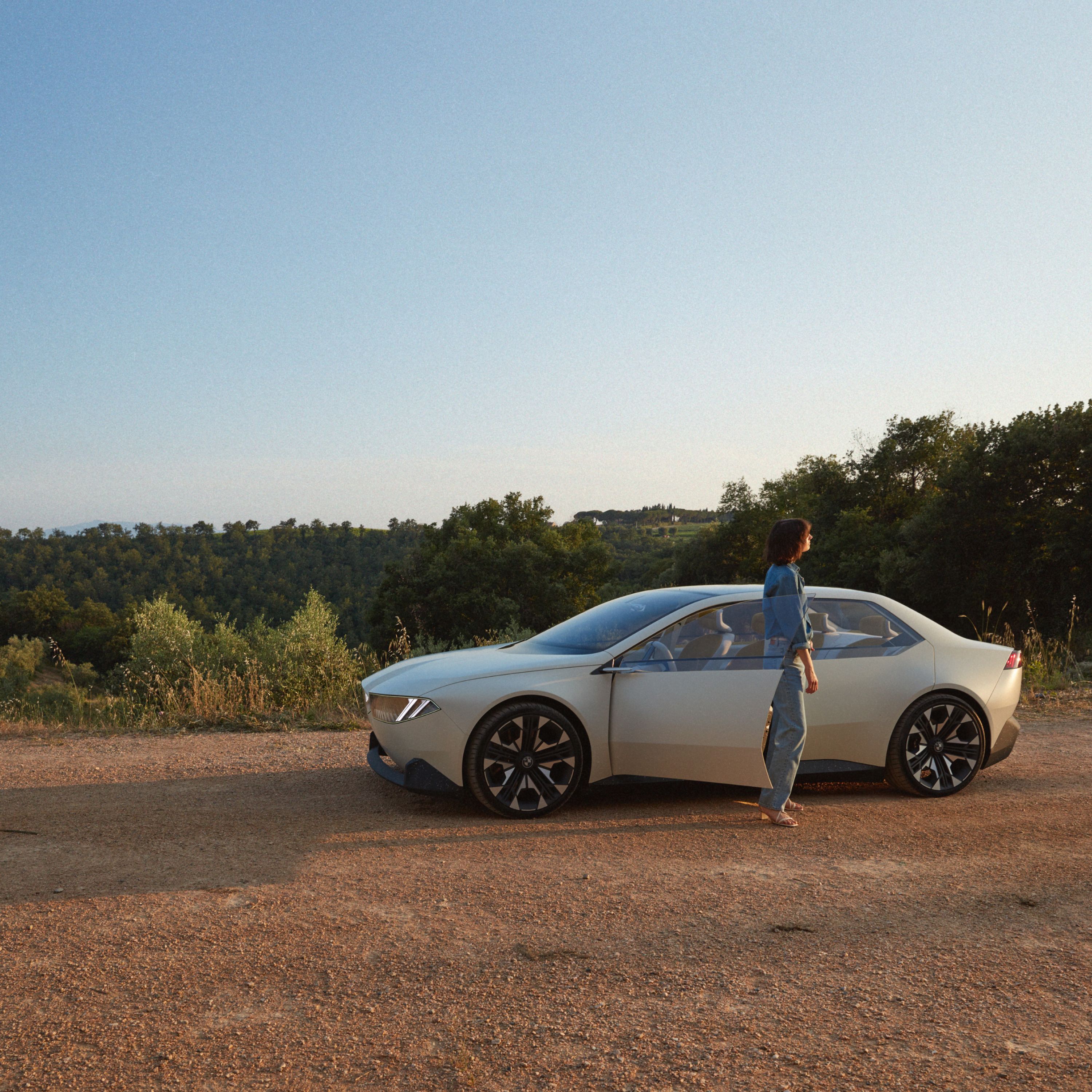 BMW Vision Neue Klasse концепт-карының сыртқы көрінісі, автокөлік ауыл жолымен қозғалып келеді.