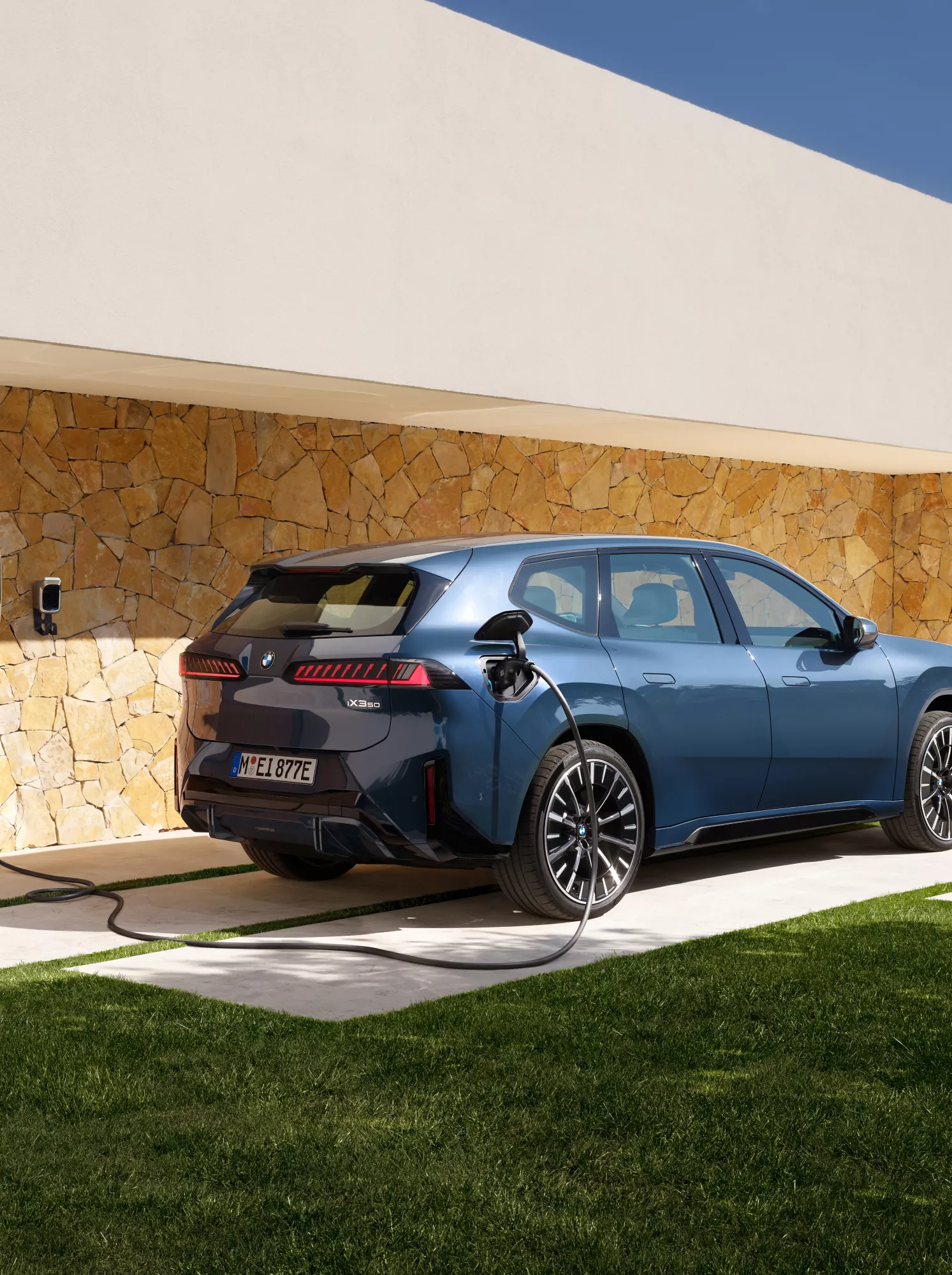 Ein BMW iX3 steht vor einem Haus mit Wallbox