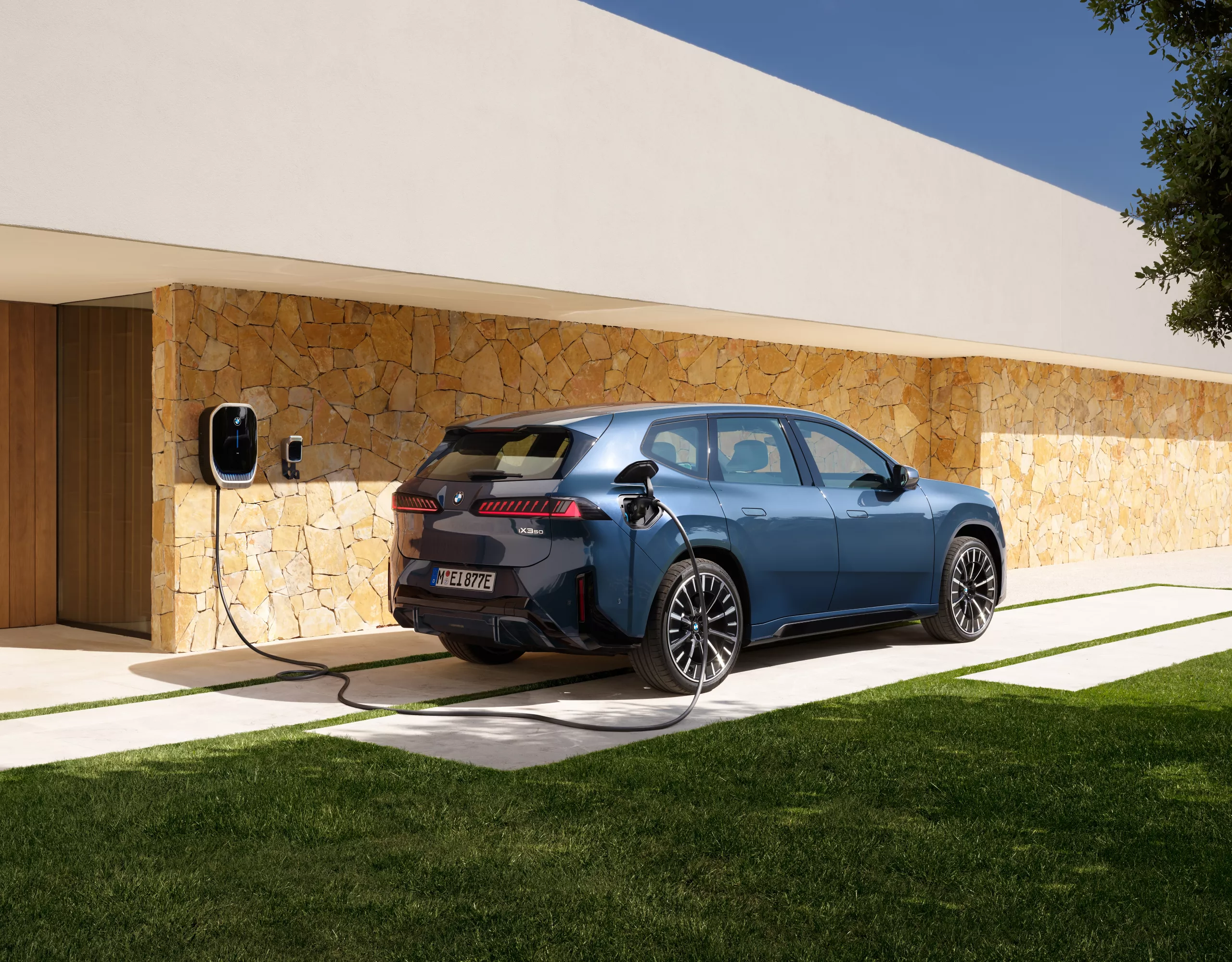 Ein BMW iX3 steht vor einem Haus mit Wallbox
