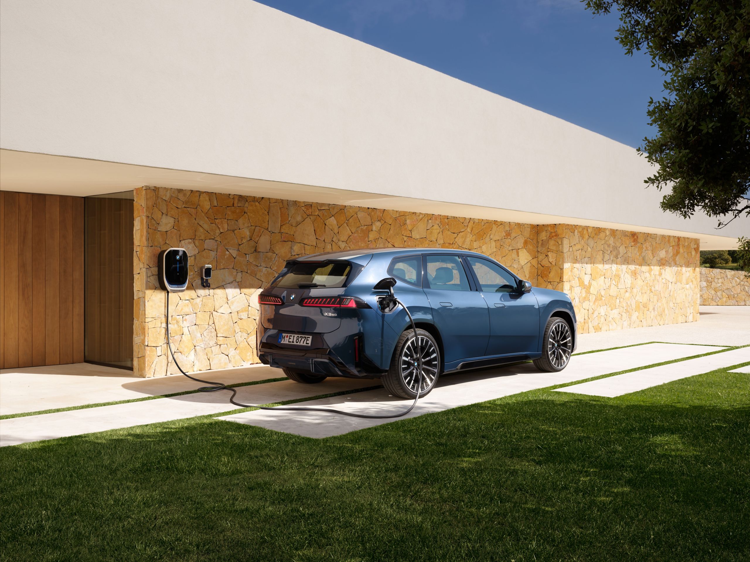 Ein BMW iX3 steht vor einem Haus mit Wallbox.
