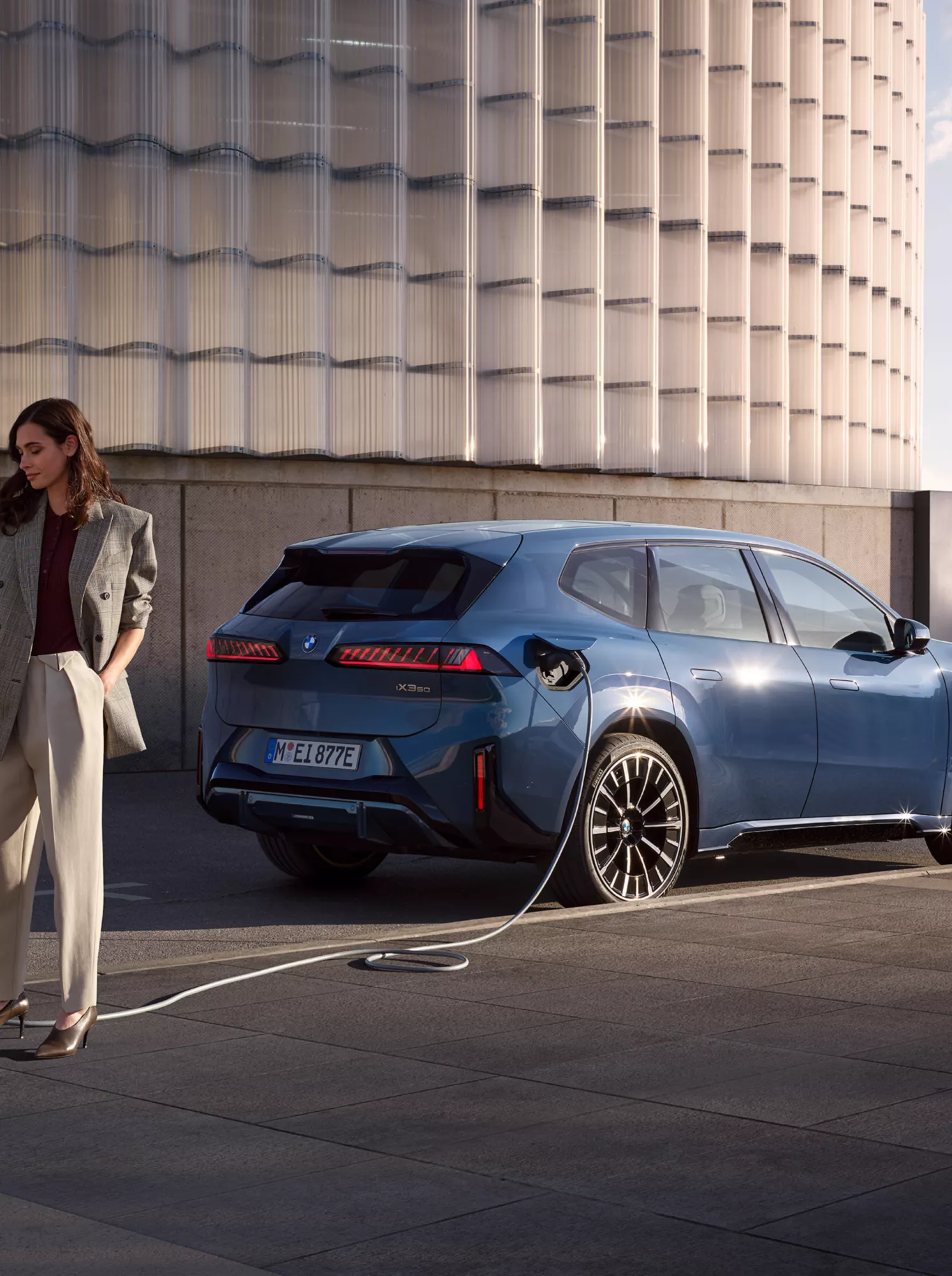 BMW iX3 připojené k veřejné nabíjecí stanici vedle osoby