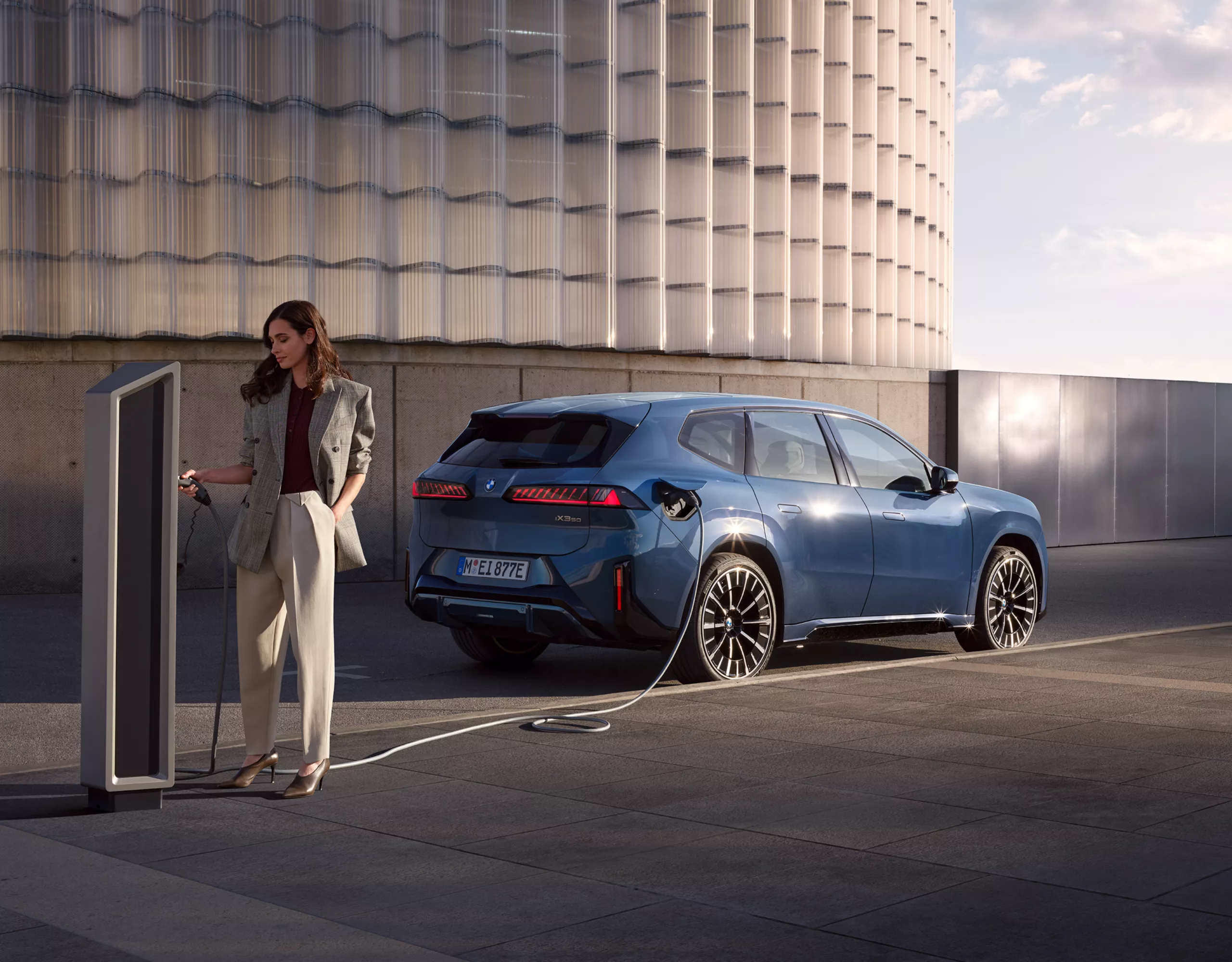 BMW iX3 branché à une borne de recharge publique près d’une personne.