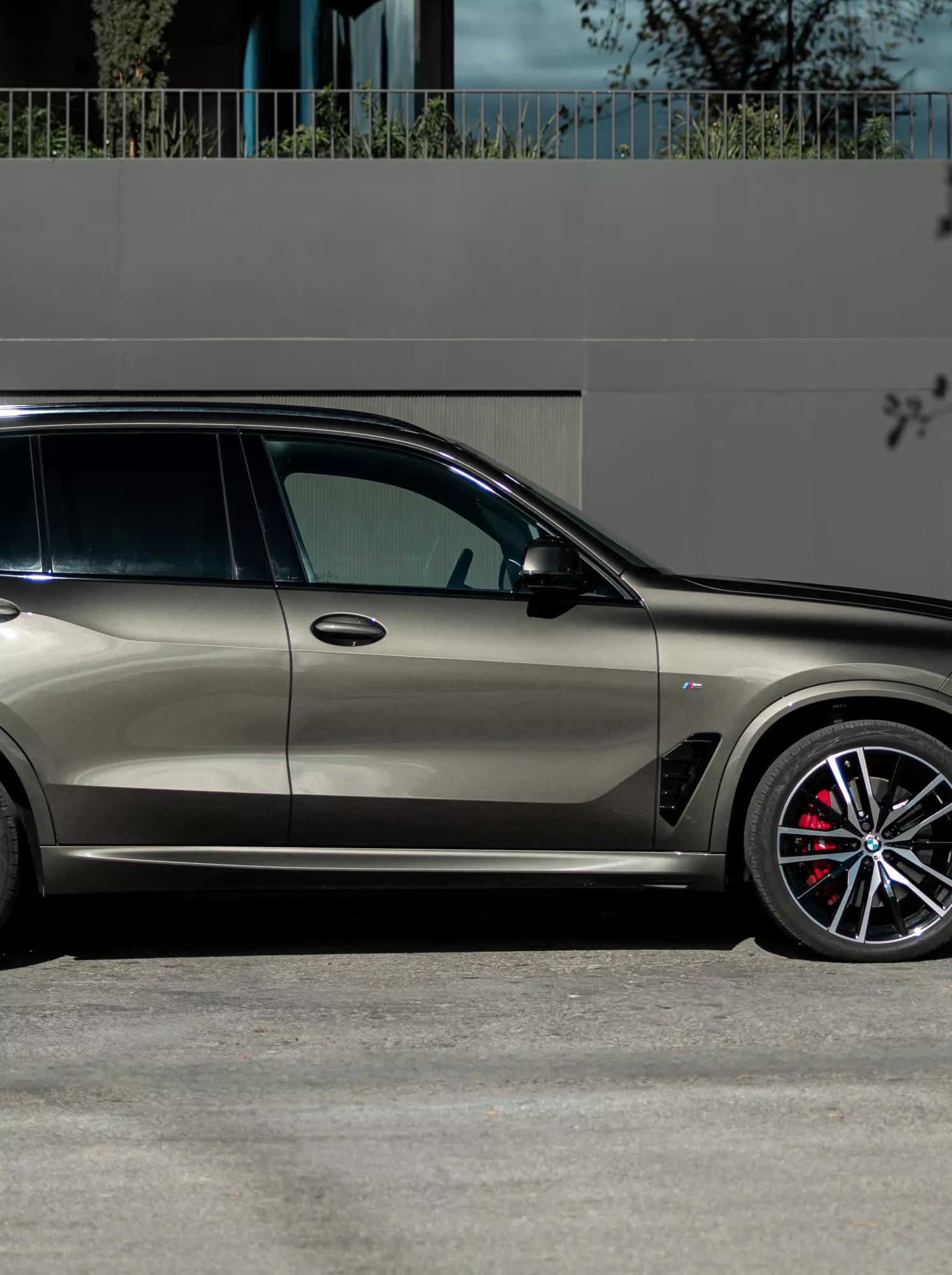 En BMW X5 står parkerad på en gata bredvid en vägg, med en person som går i närheten.