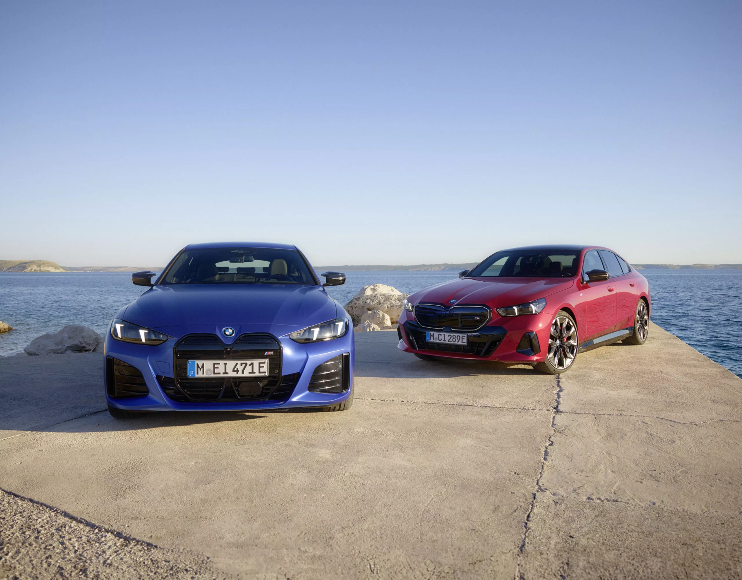 Dos vehículos BMW, uno azul y otro rojo, junto al mar 