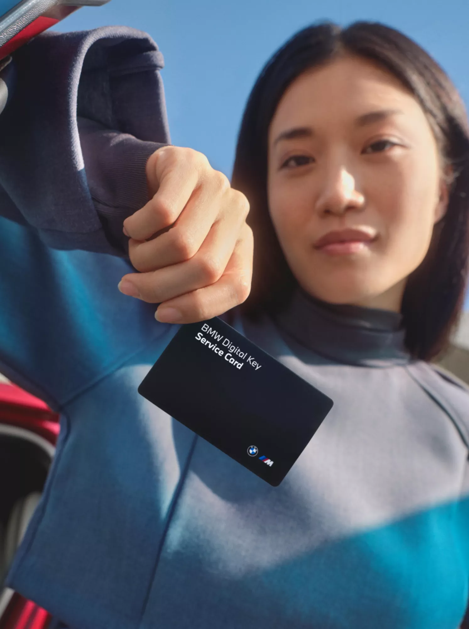 Žena se opírá o dveře vozu a ukazuje kartu Service Card klíče BMW Digital Key