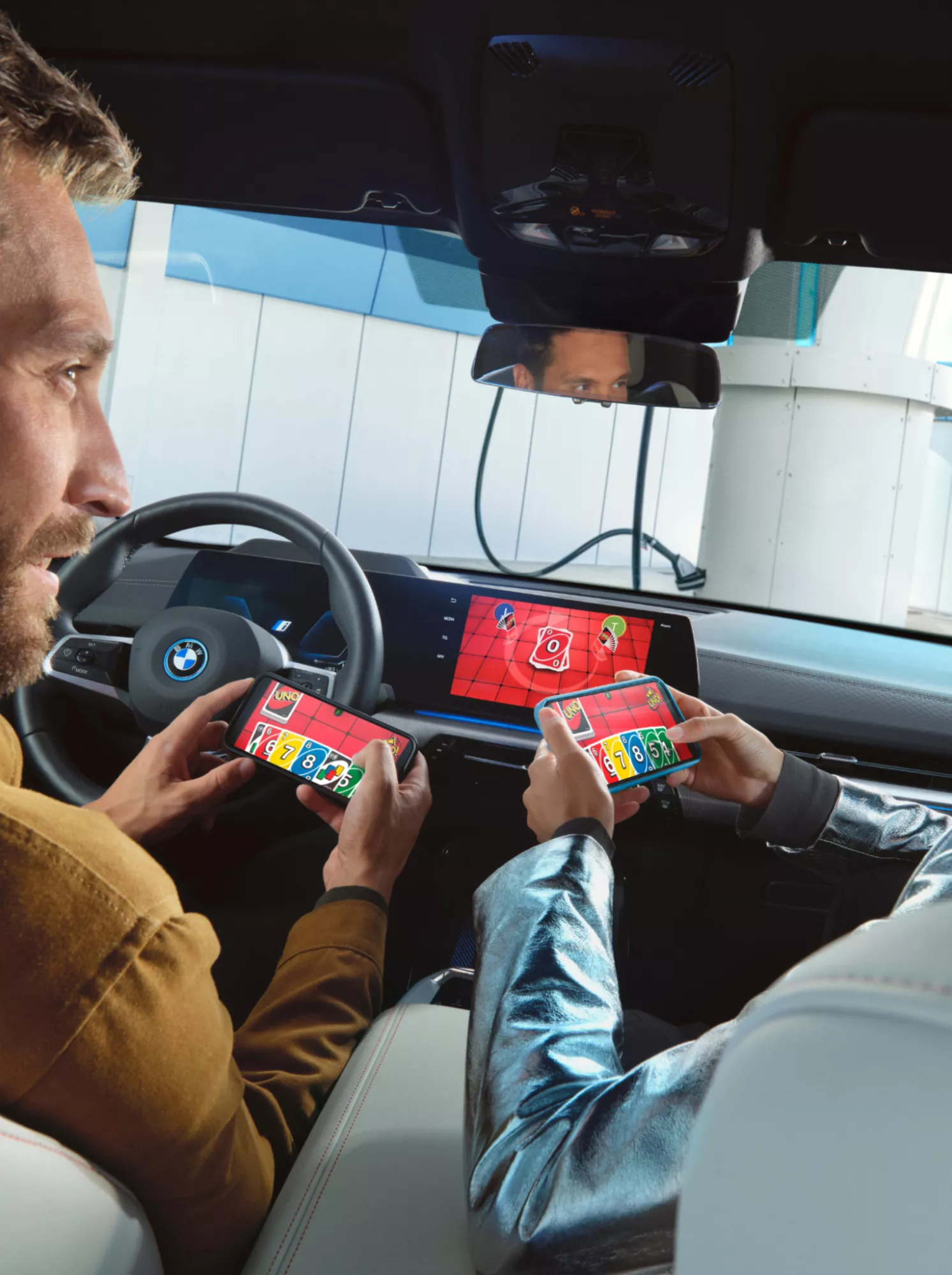 Du žmonės savo BMW automobilyje žaidžia žaidimą naudodamiesi išmaniuoju telefonu ir centriniu ekranu
