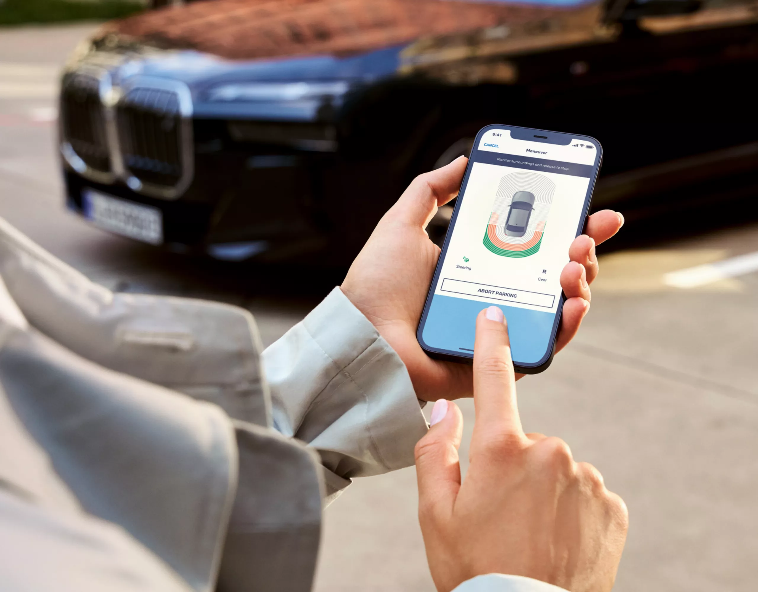Se utiliza un smartphone con la aplicación My BMW para aparcar un BMW visible en segundo plano