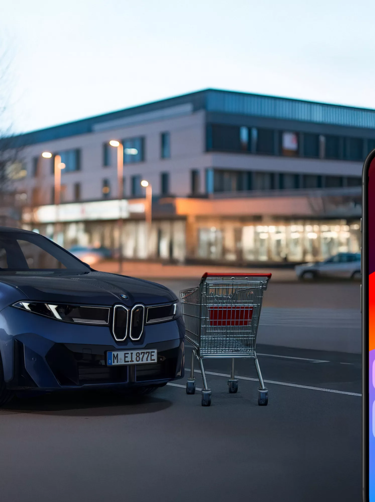 Smartphone mit My BMW Benachrichtung von Parkschäden. Im Hintergrund stellt ein parkender BMW die Kollision mit einem Einkaufswagen dar