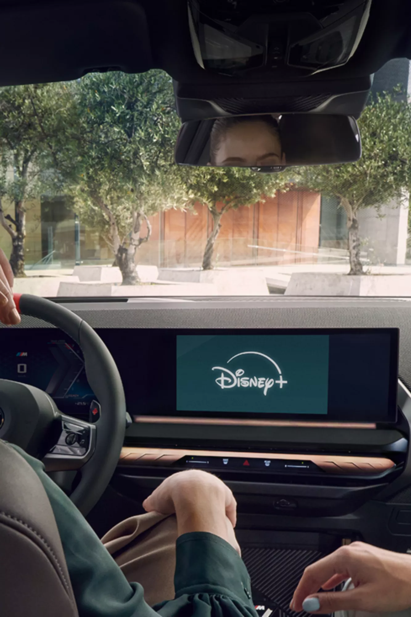 Dos mujeres están sentadas sonriendo en el puesto de conducción de un BMW. La aplicación Disney+ está abierta en la pantalla central