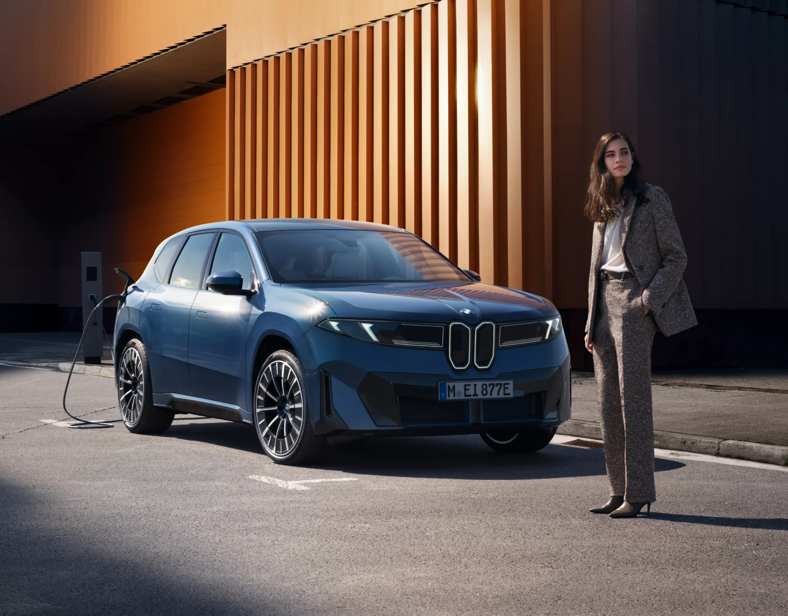 A person is standing in front of a BMW electric vehicle that is charging at the side of the road
