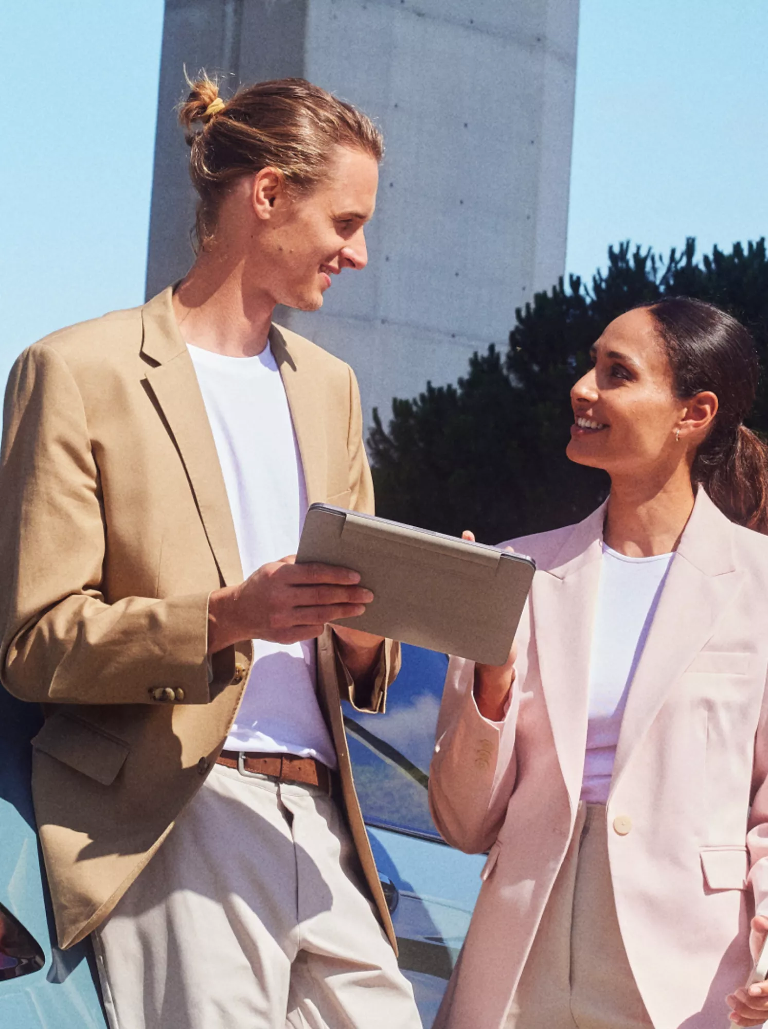 A person with a clipboard is leaning against a BMW and talking to another person