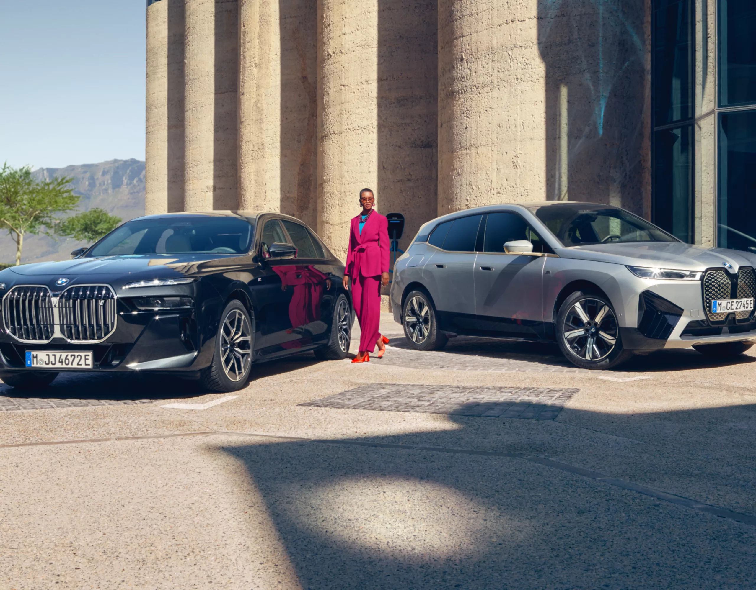 A person is standing between two BMWs parked in front of an imposing entrance