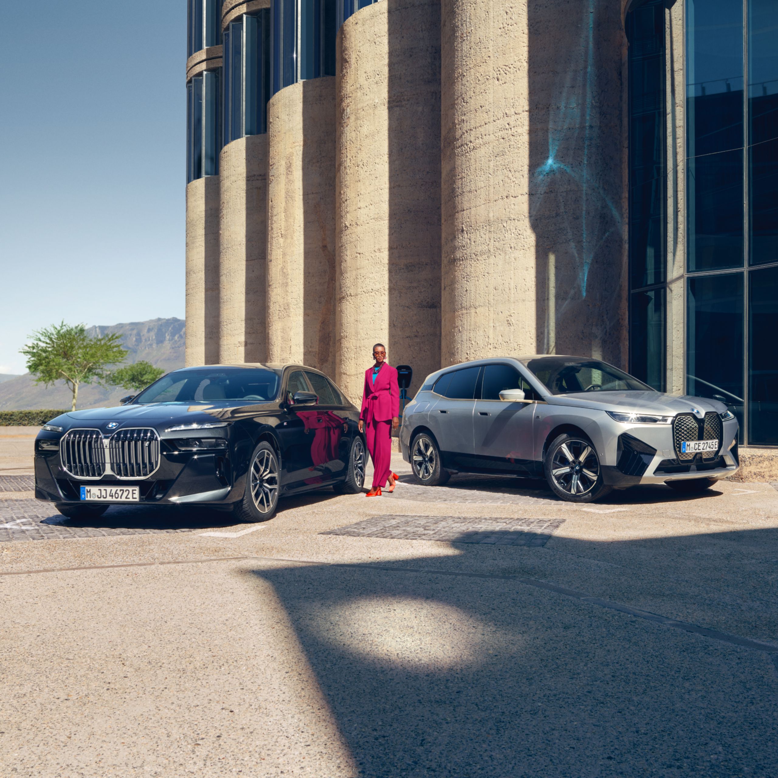 A person is standing between two BMWs parked in front of an imposing entrance