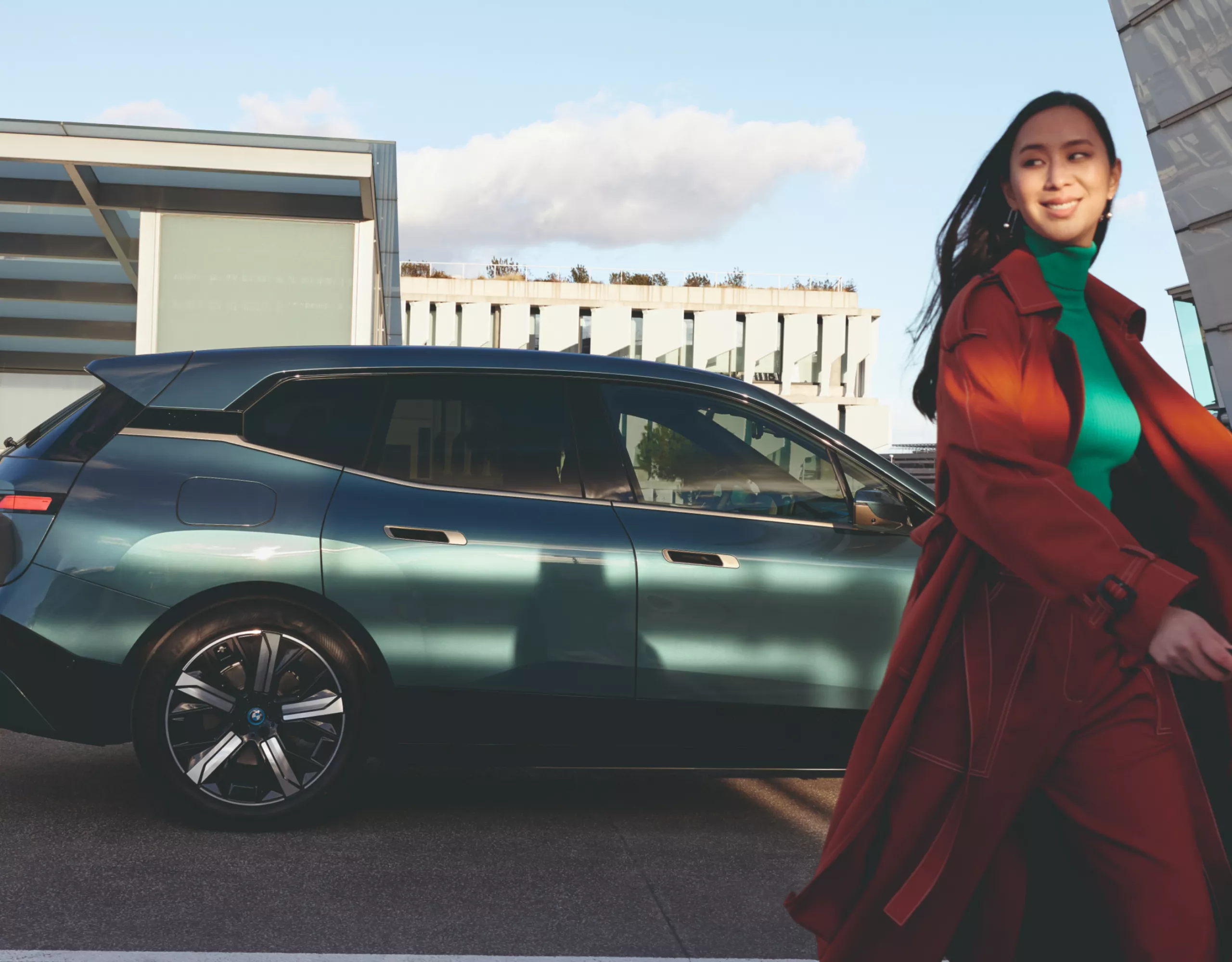 Person walking away from a BMW parked in front of a building with a flat roof