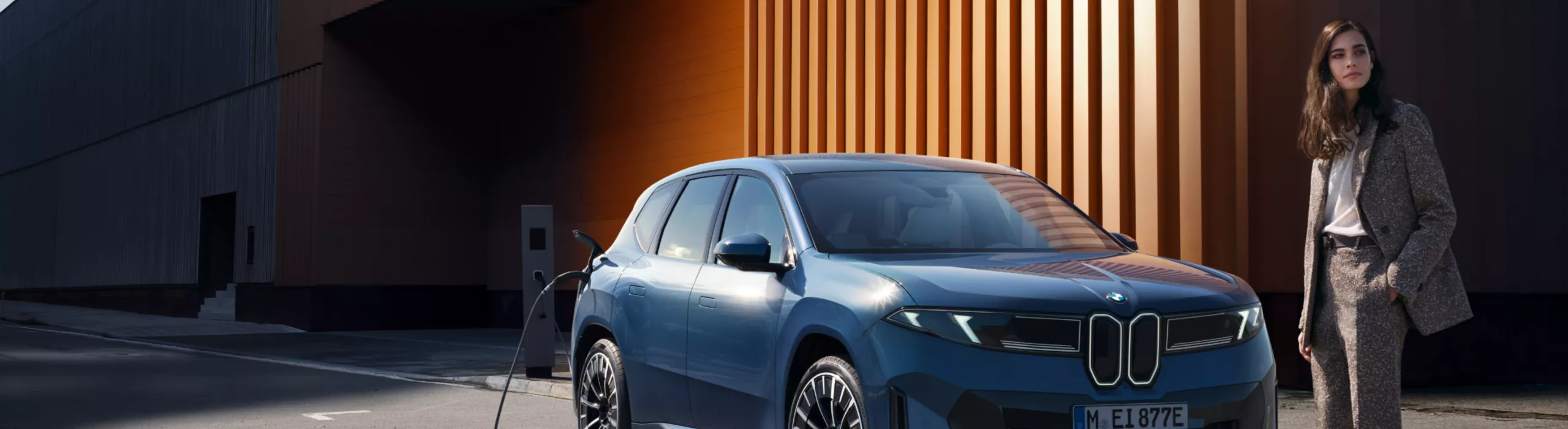 A person is standing in front of a BMW electric vehicle that is charging at the side of the road
