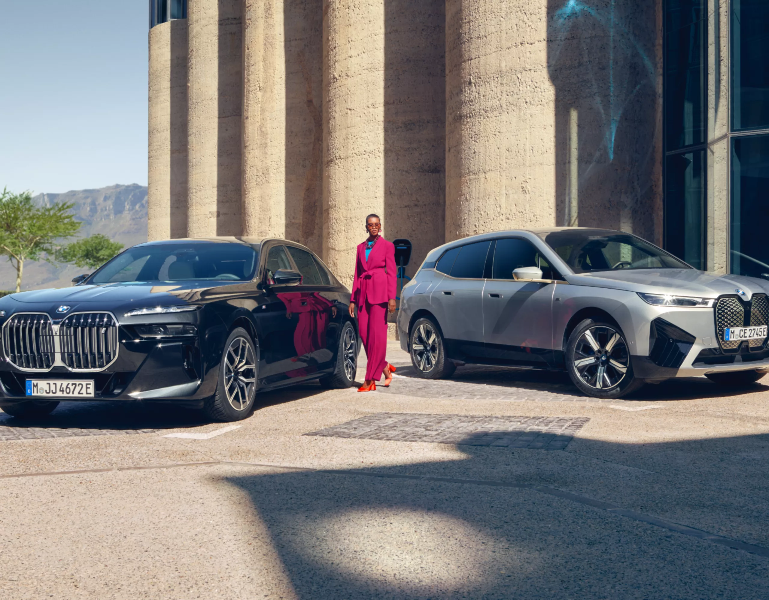 A woman is standing between two fully electric BMW vehicles in front of a building