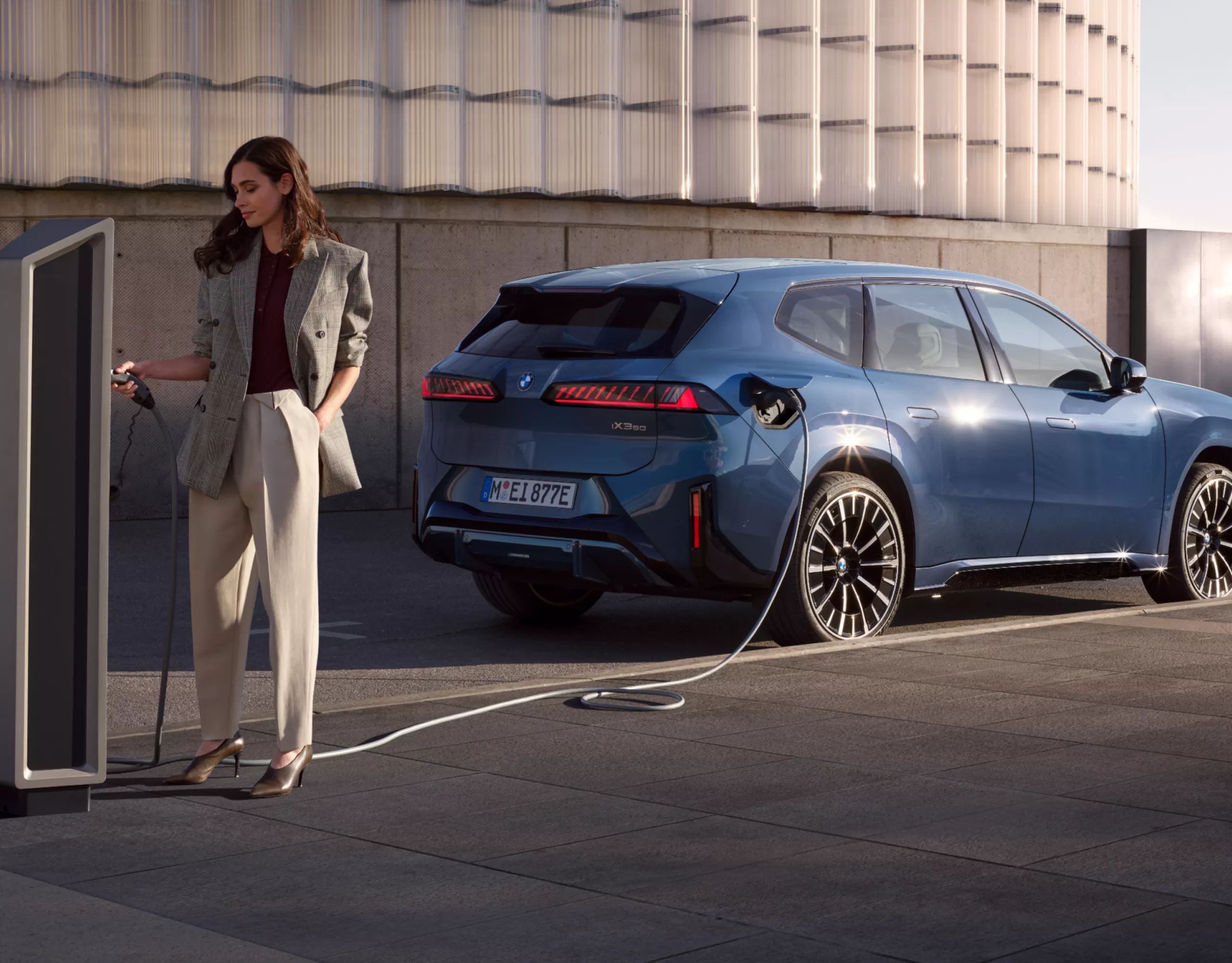 A person looks at the charging station where a BMW electric vehicle is charging in the background