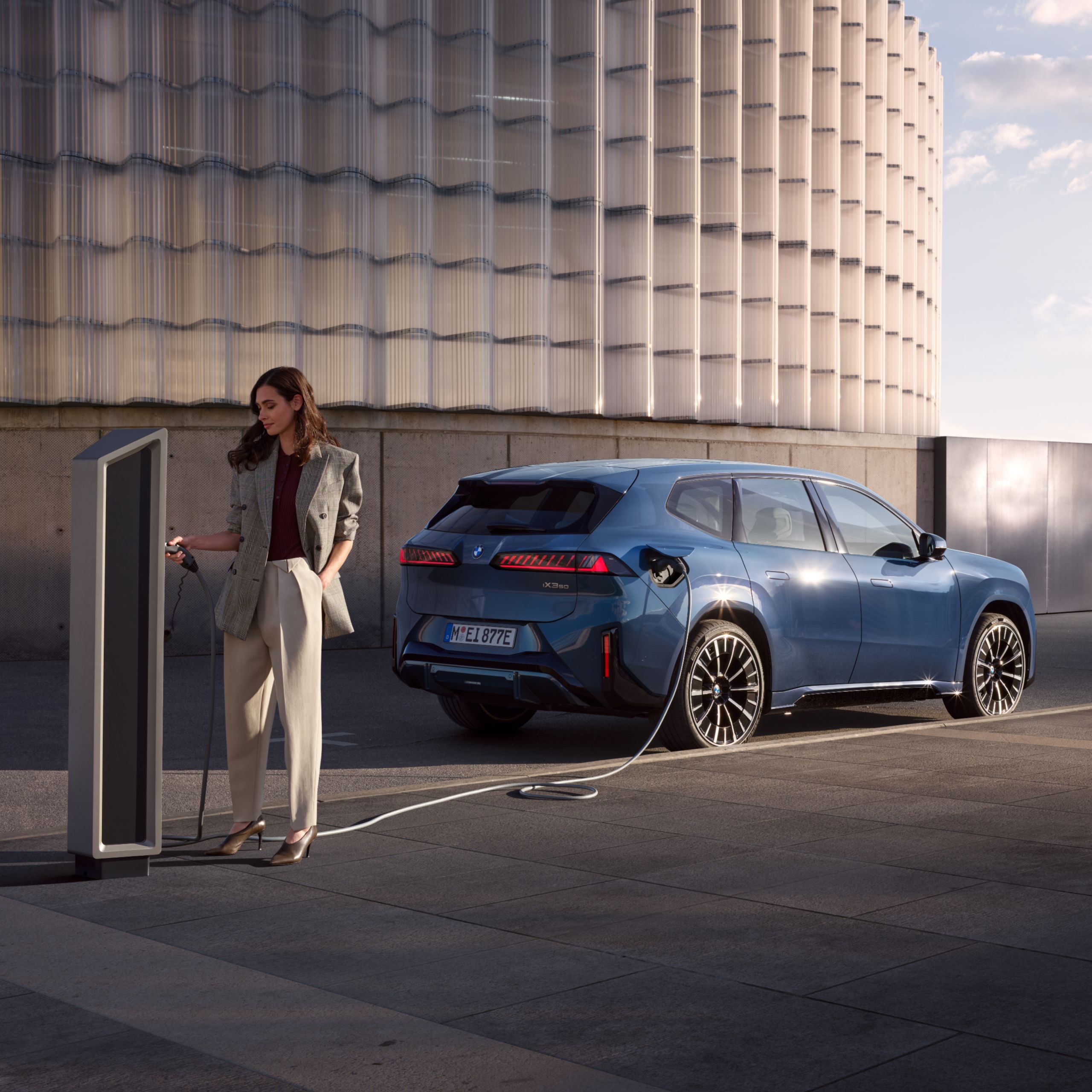A person looks at the charging station where a BMW electric vehicle is charging in the background