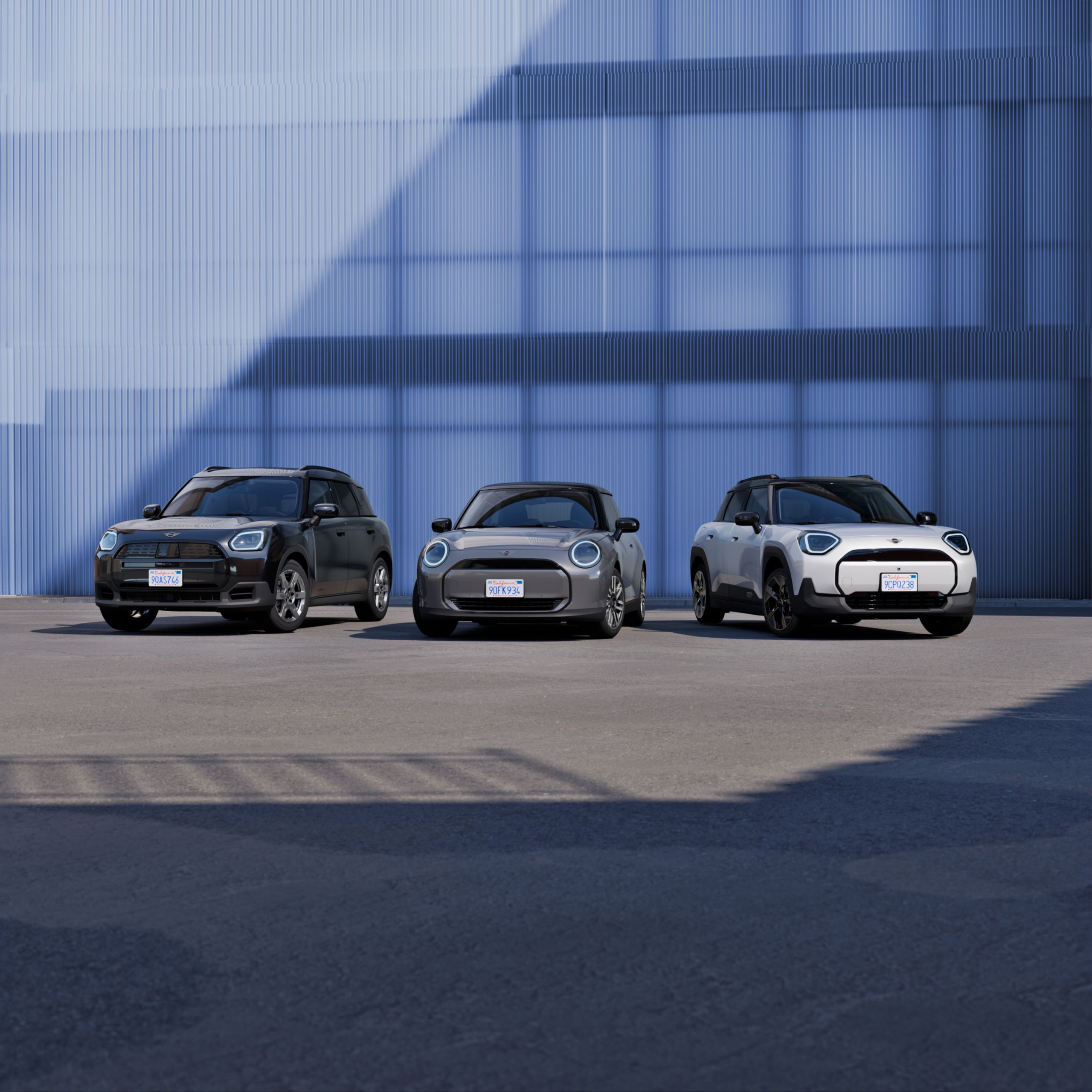 Three MINIs are parked on grey concrete in front of a blue corrugated wall