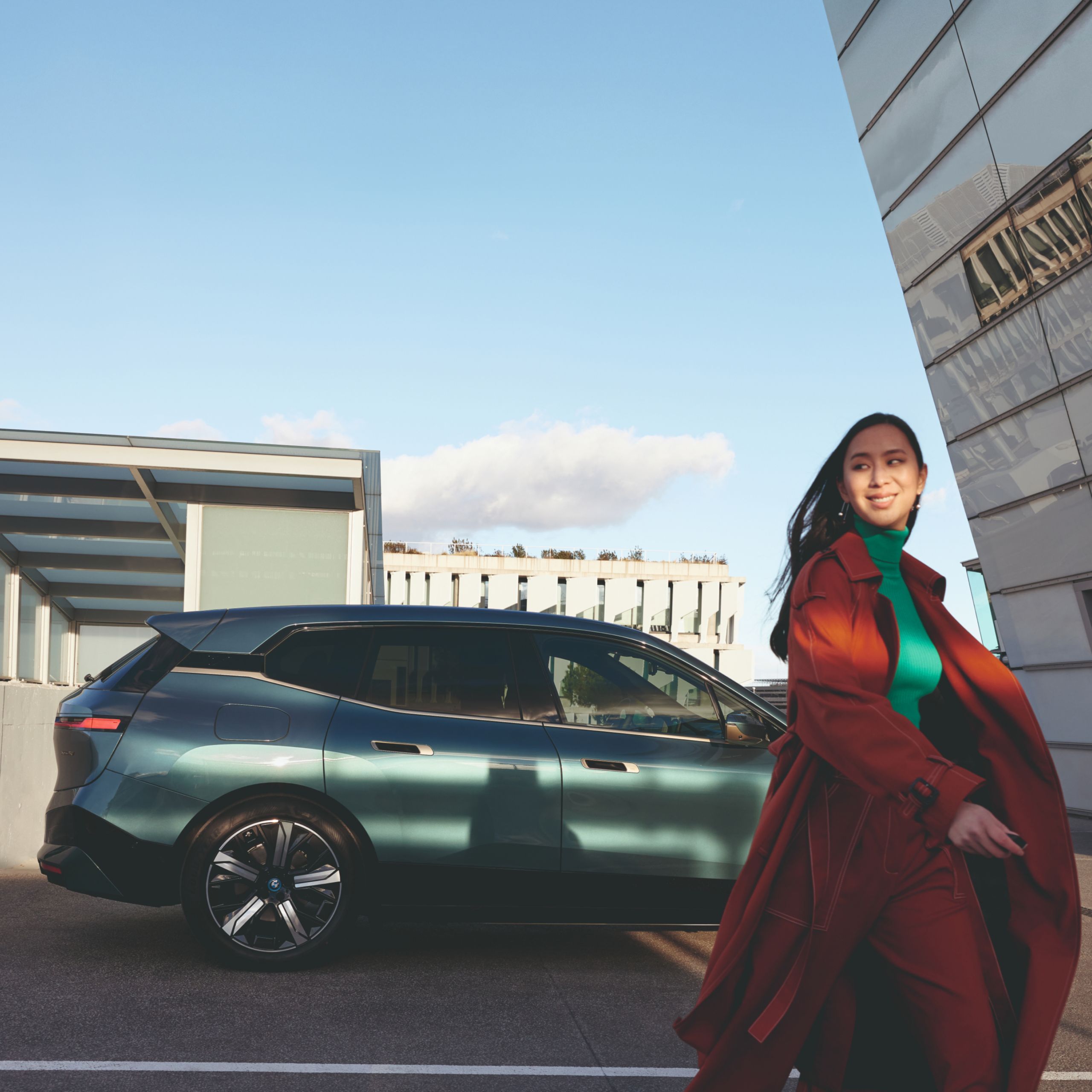 Person walking away from a BMW parked in front of a building with a flat roof