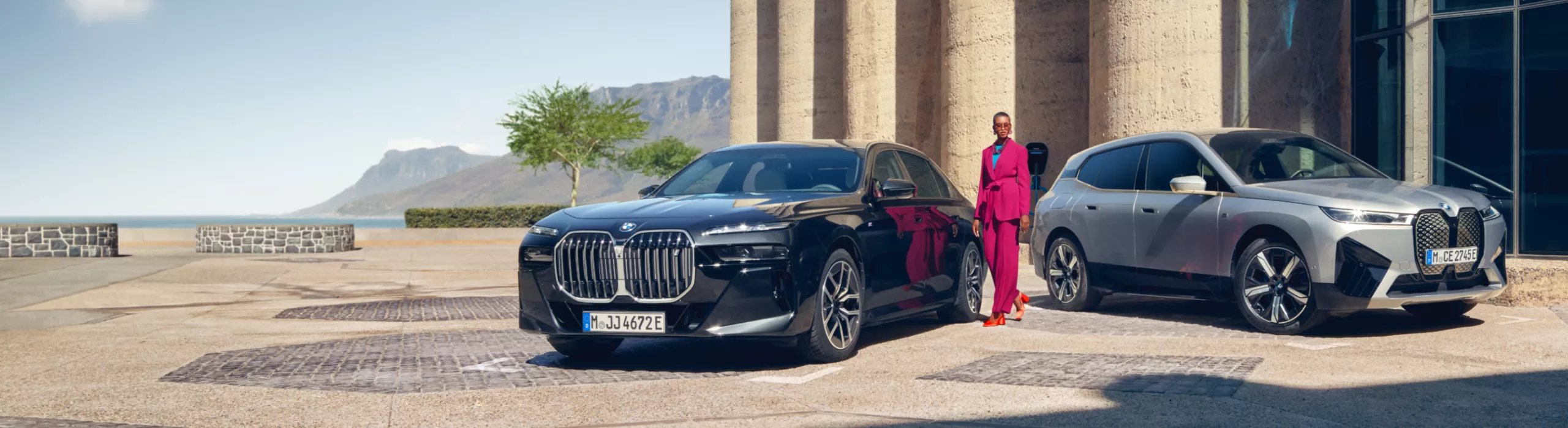 A person stands between a BMW saloon and a BMW SUV in front of an entrance area flanked by columns