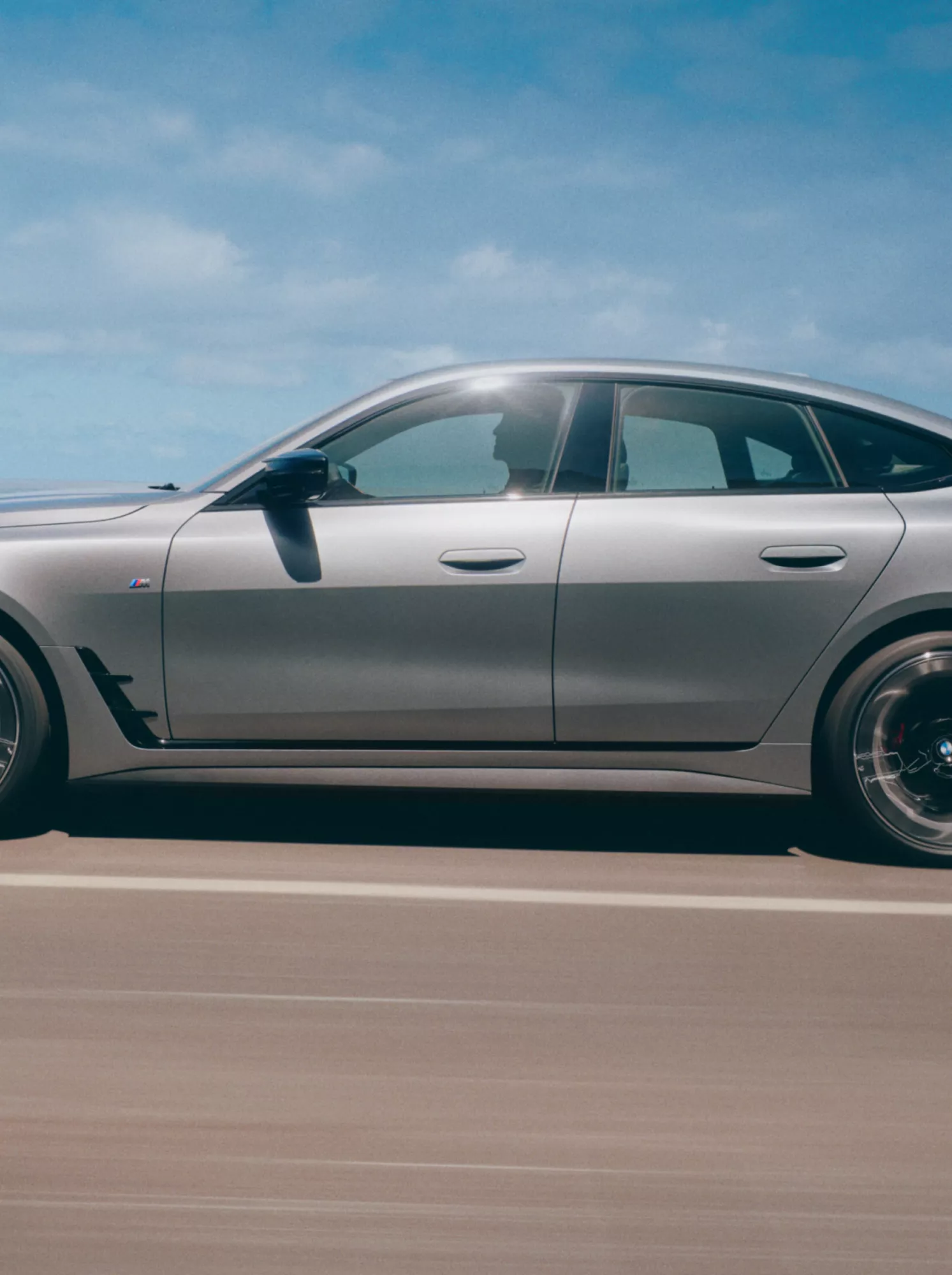 Een grijze BMW in zijaanzicht rijdt op een weg aan zee