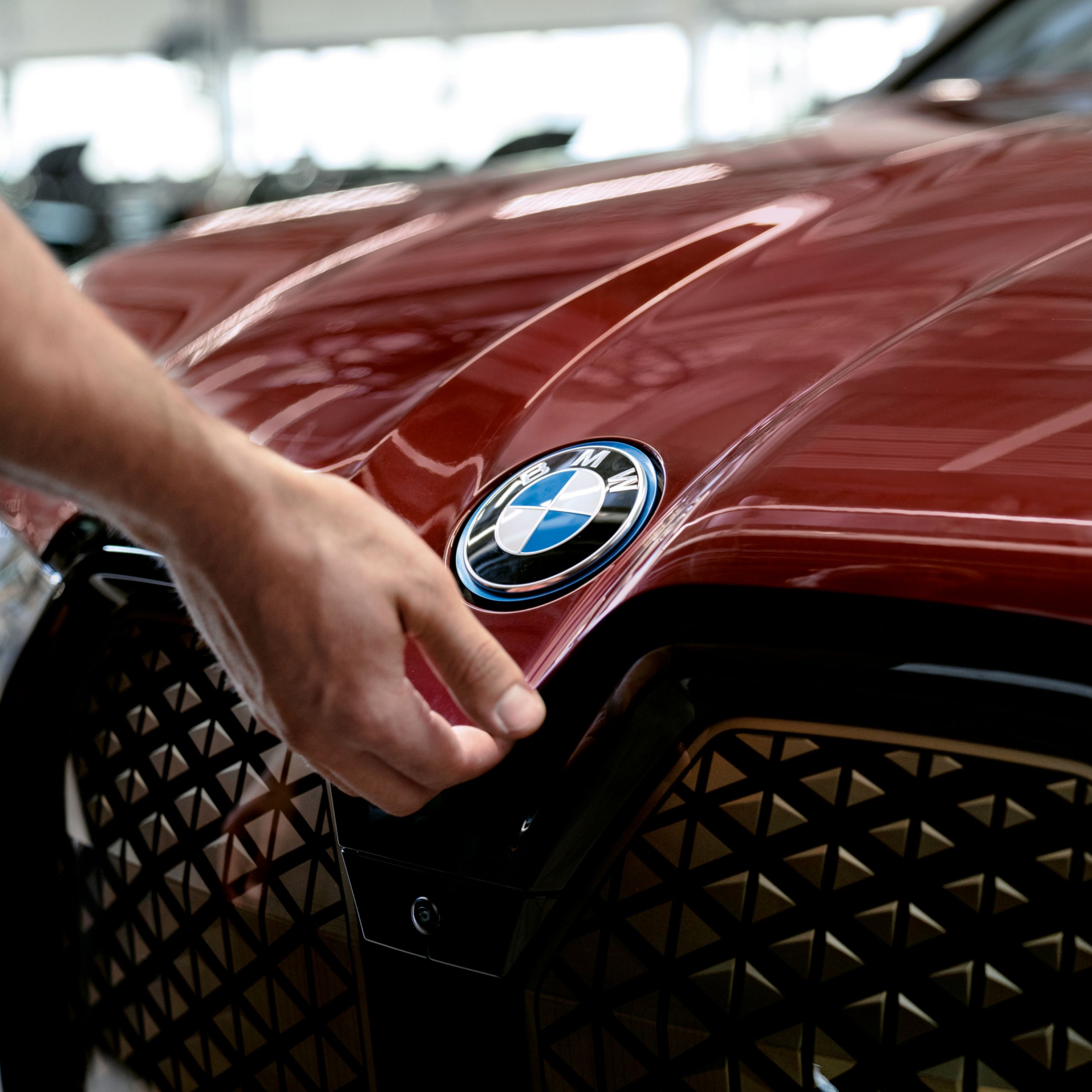 Eine Hand fasst an das blau umrandete BMW Emblem auf der Vorderseite eines roten BMW.