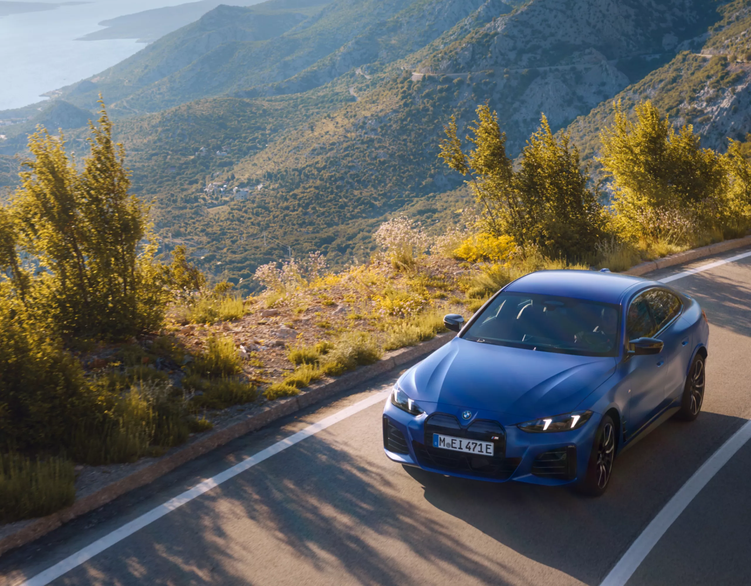 A blue BMW drives along a coastal landscape. The BMW is seen from the front 
