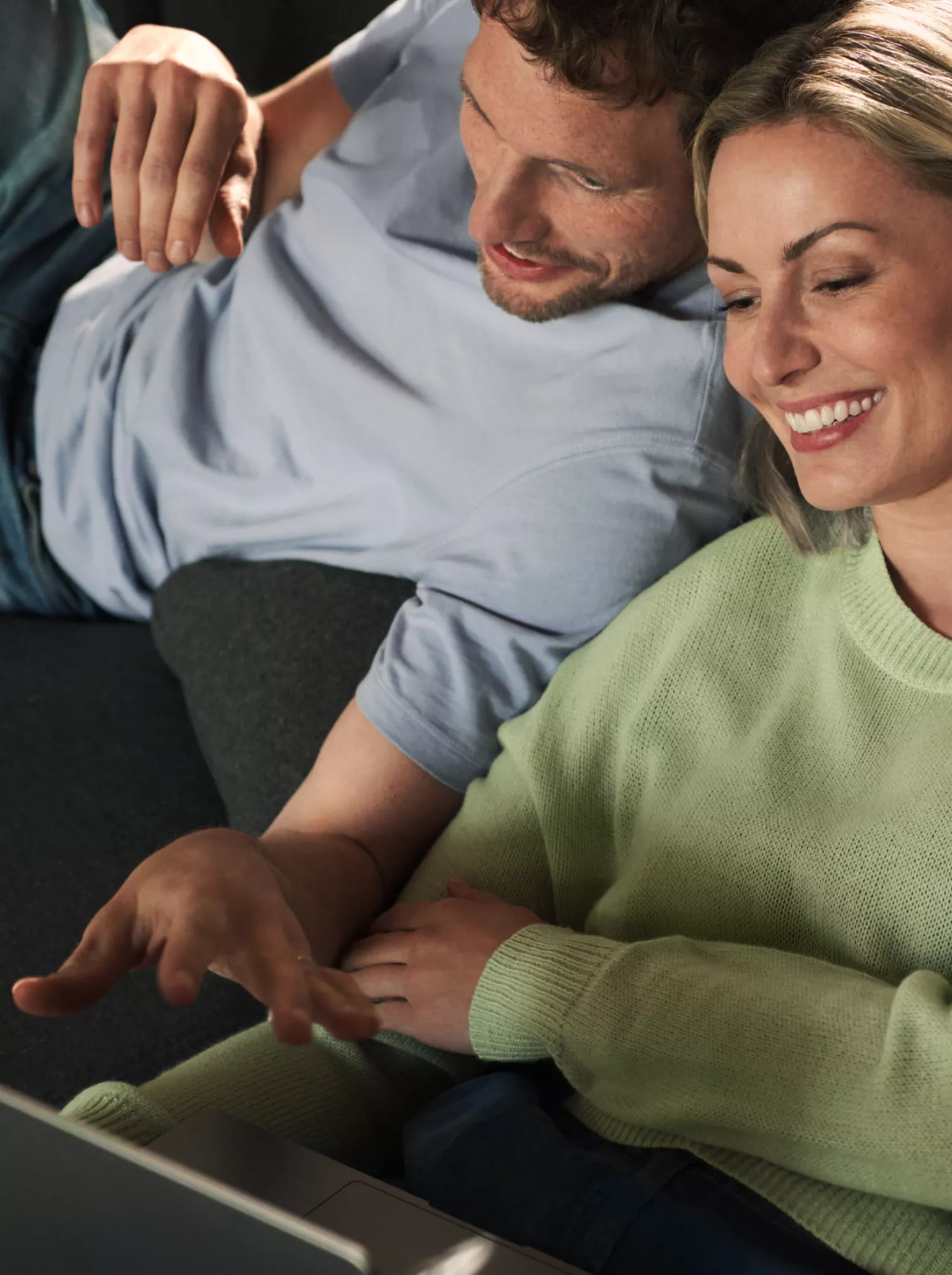 Zwei Personen schauen auf einen Laptop. Sie sitzen gemütlich auf dem Sofa