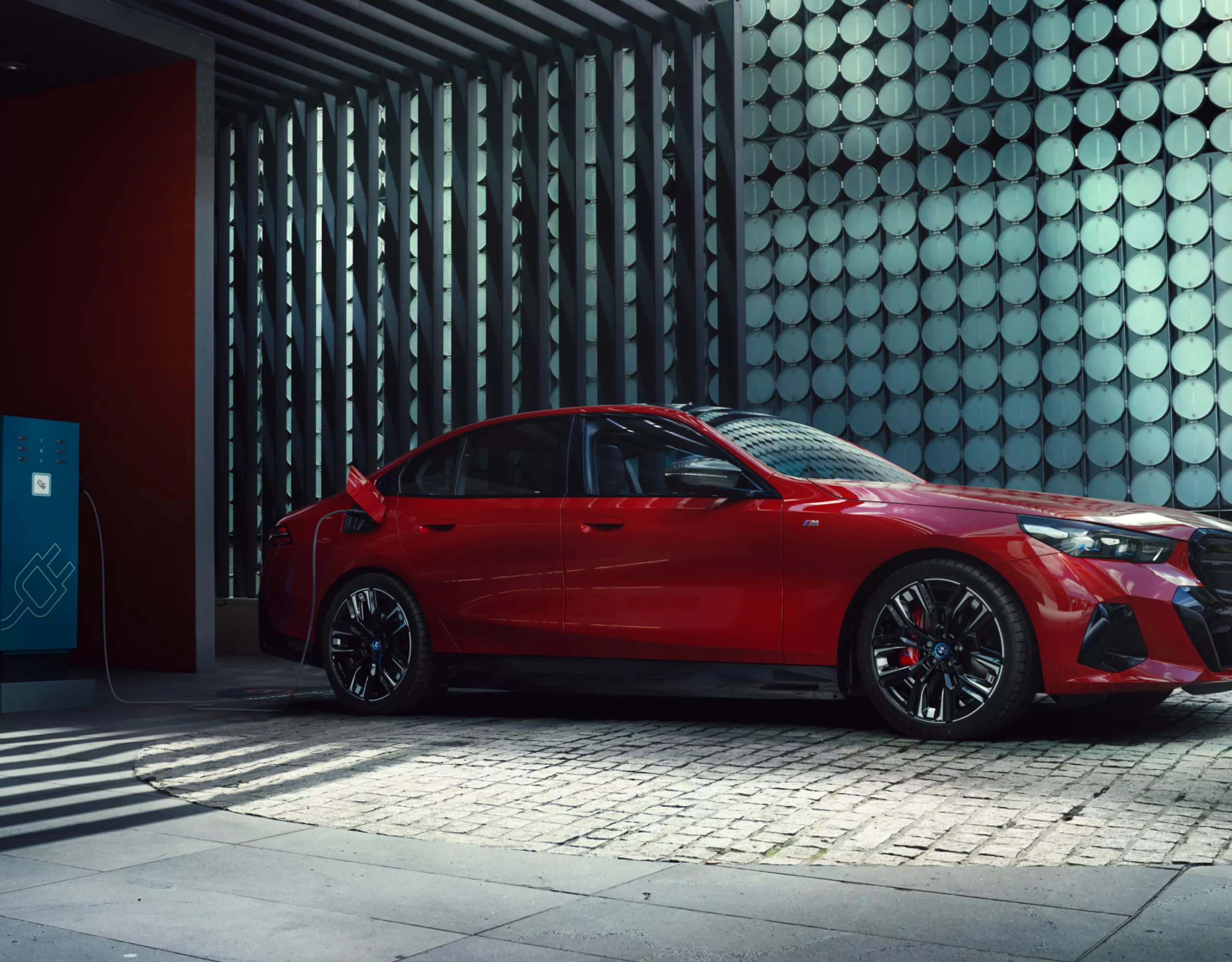 A red BMW electric vehicle stands in front of a futuristic wall